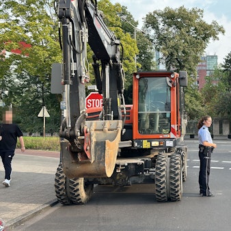 Eine Polizistin steht vor einem Bagger auf einer Straße.