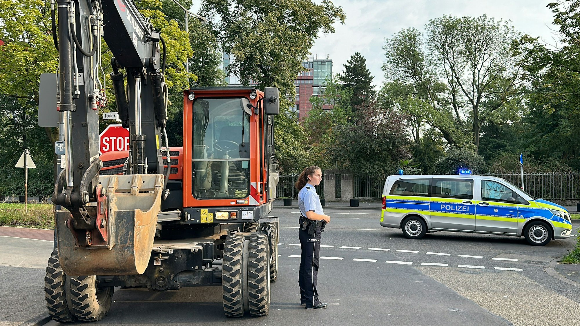 Eine Polizistin steht vor einem Bagger auf einer Straße.