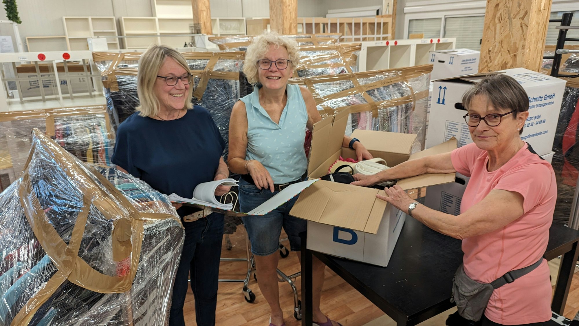 Zwei Frauen packen einen Karton, eine schaut in eine Liste vor leer geräumten Regalen.