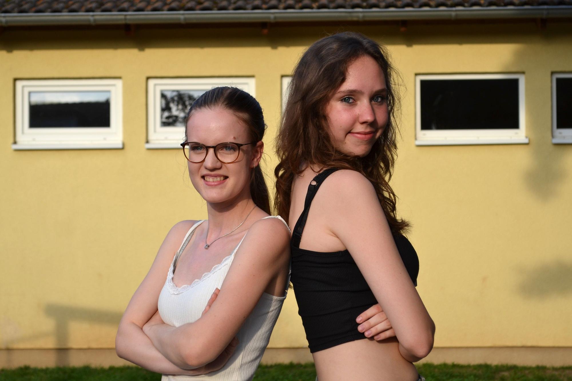 Zwei junge Frauen stehen Rücken an Rücken und schauen in die Kamera.