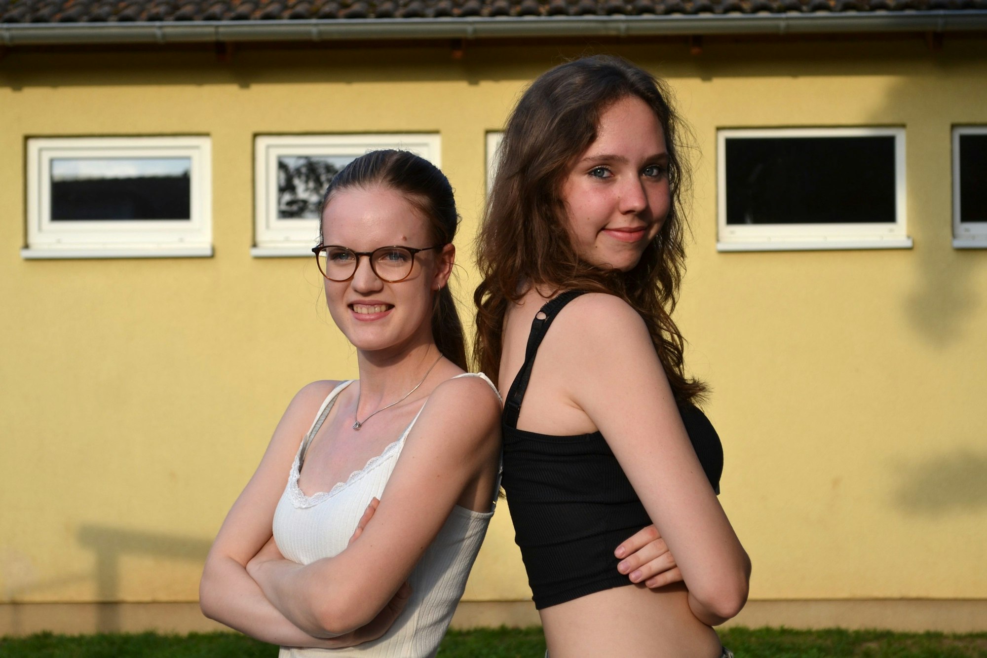 Zwei junge Frauen stehen Rücken an Rücken und schauen in die Kamera.