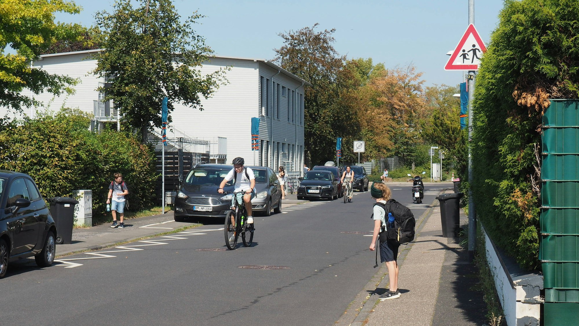 Das Foto zeigt Radfahrer vor einer Schule und Kinder auf ihrem Heimweg.
