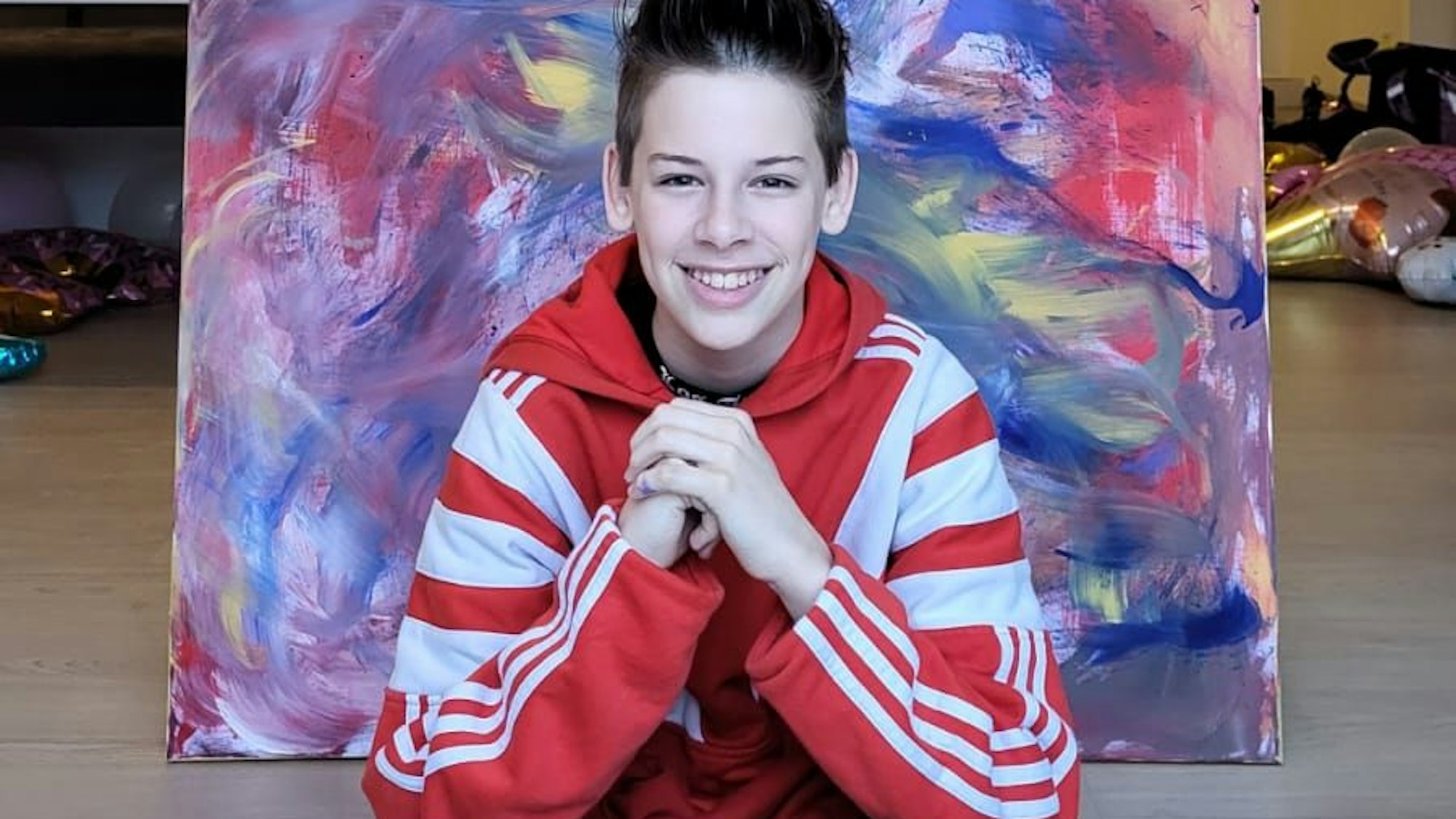 Ein Junge sitzt auf dem Boden vor einem bunten abstrakten Bild.
