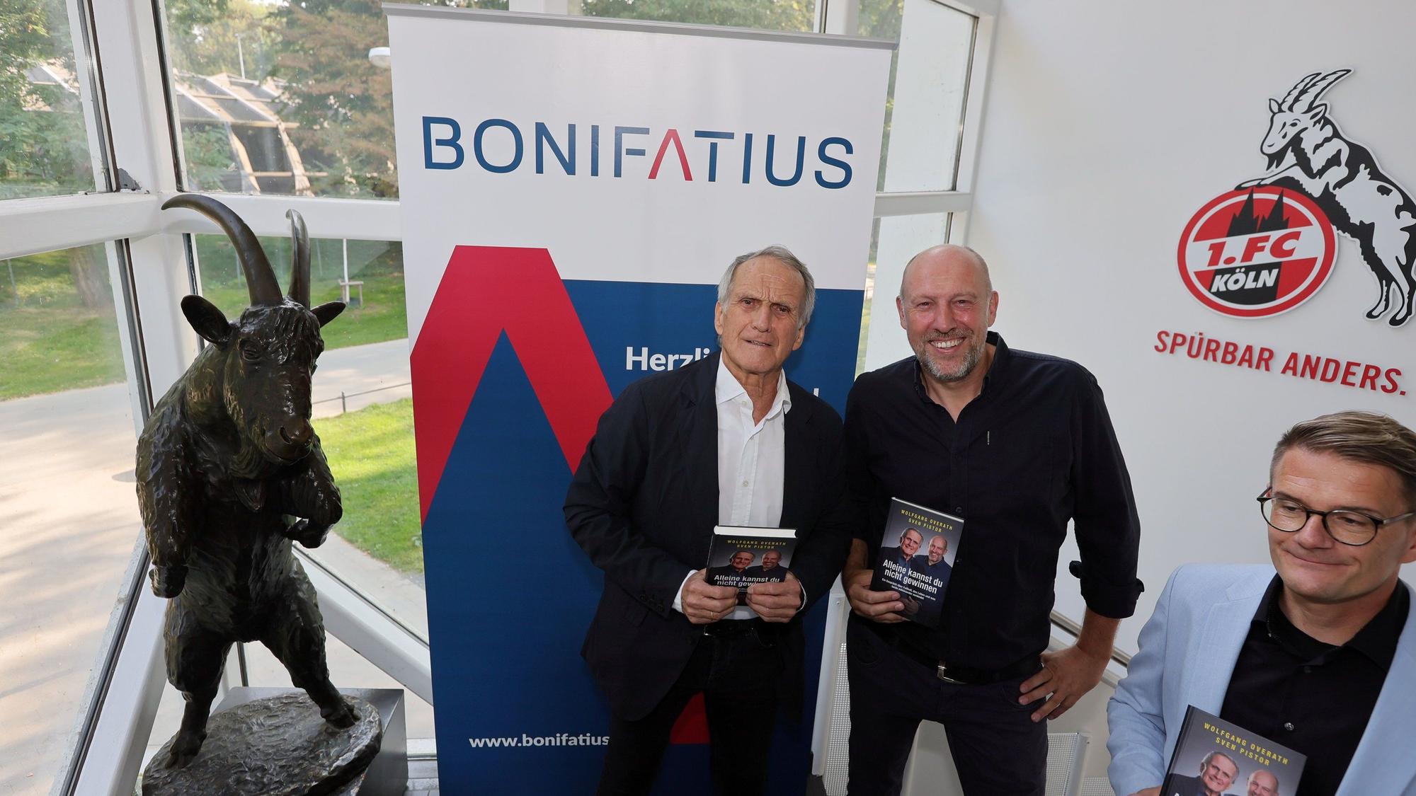 Drei Männer stehen nebeneinander und halten Bücher in den Händen.
