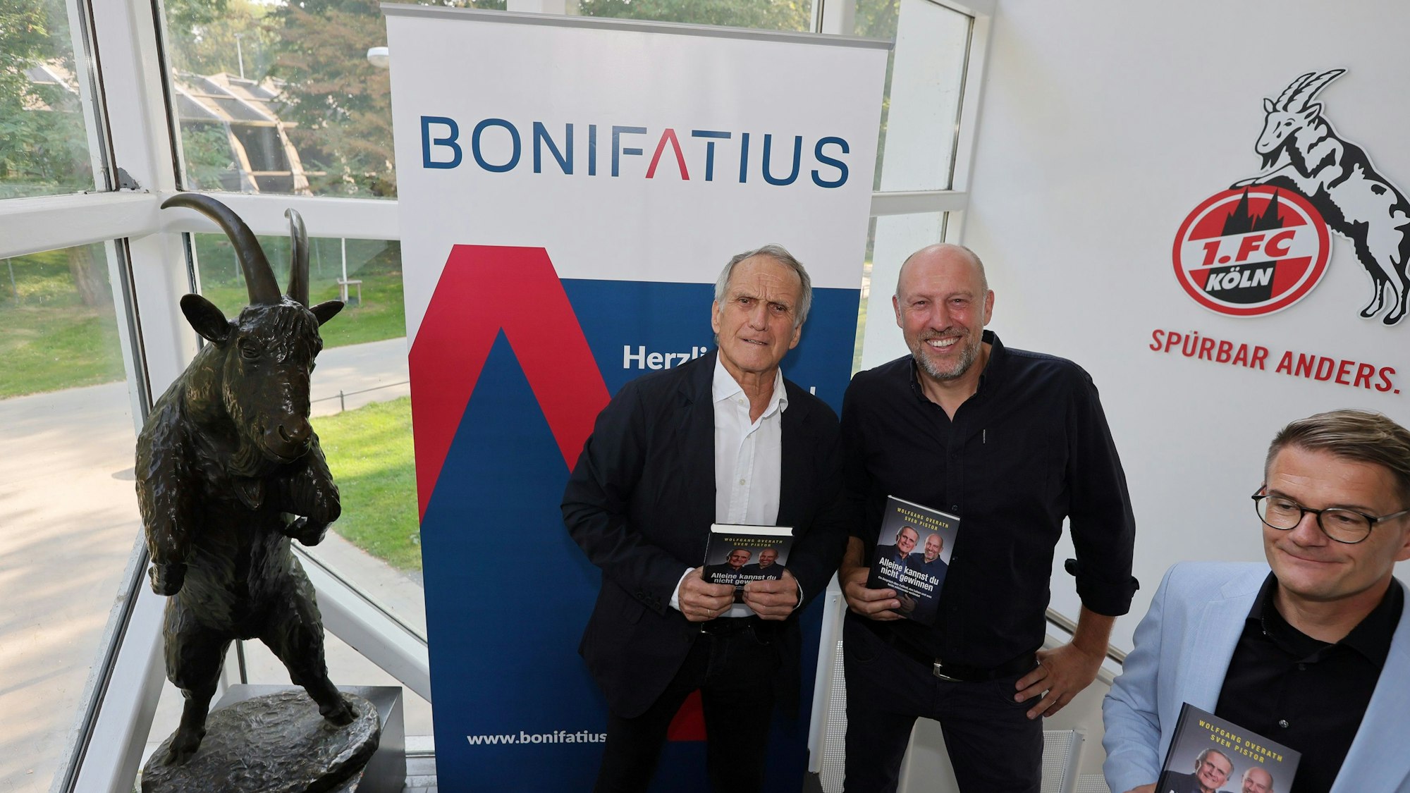 Drei Männer stehen nebeneinander und halten Bücher in den Händen.