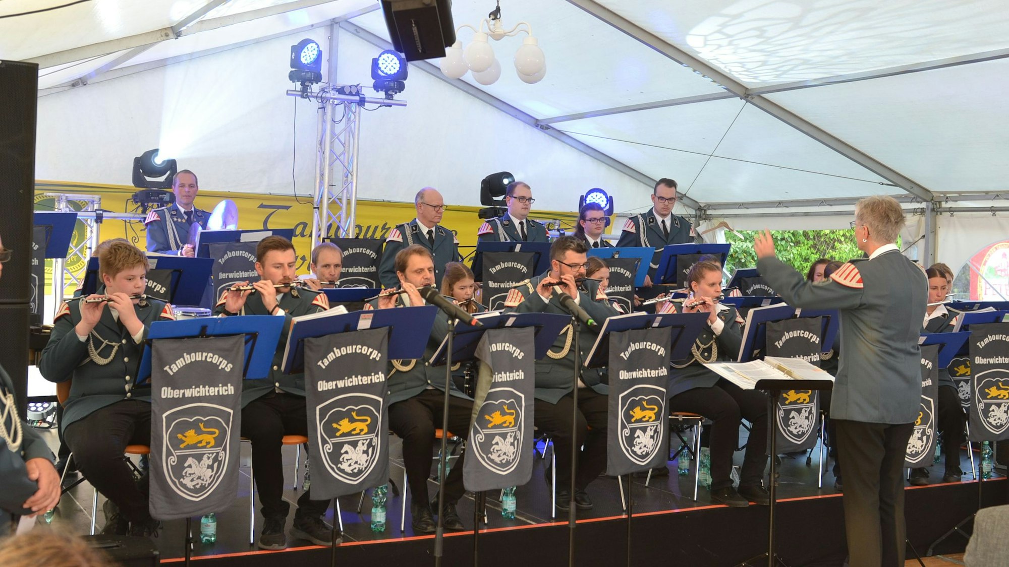 Die Aktiven des Tambourcorps Oberwichterich sitzen bei einem Konzert auf der Bühne in einem Festzelt.