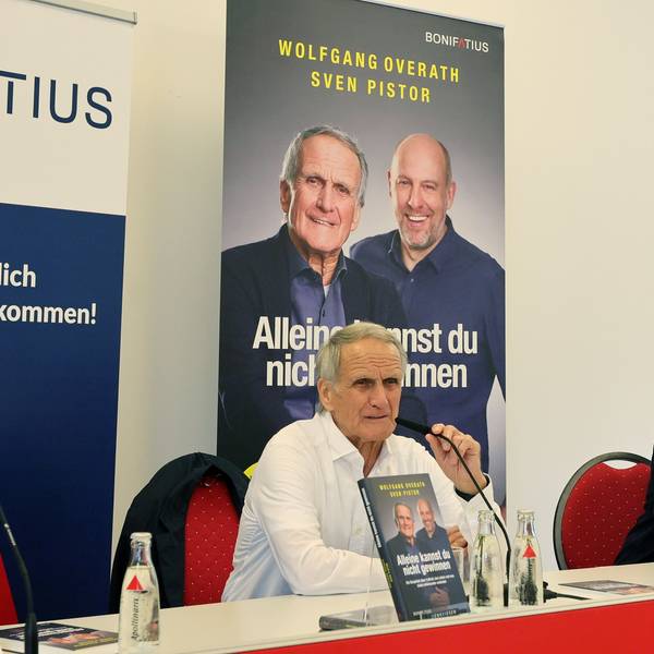 Zwei Männer sitzen an einem Tisch nebeneinander.