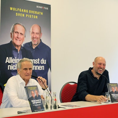 Zwei Männer sitzen an einem Tisch nebeneinander.