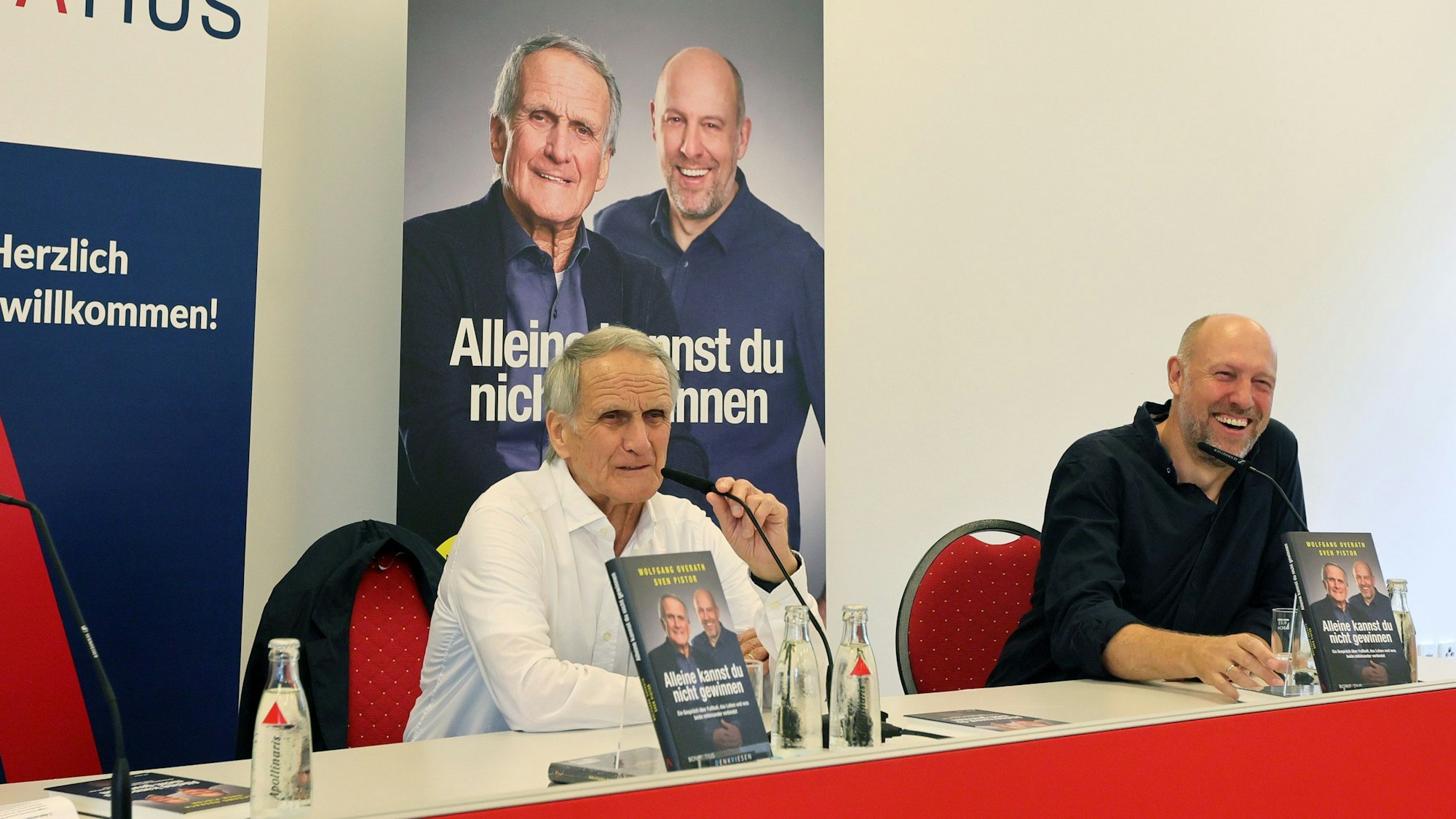 Zwei Männer sitzen an einem Tisch nebeneinander.