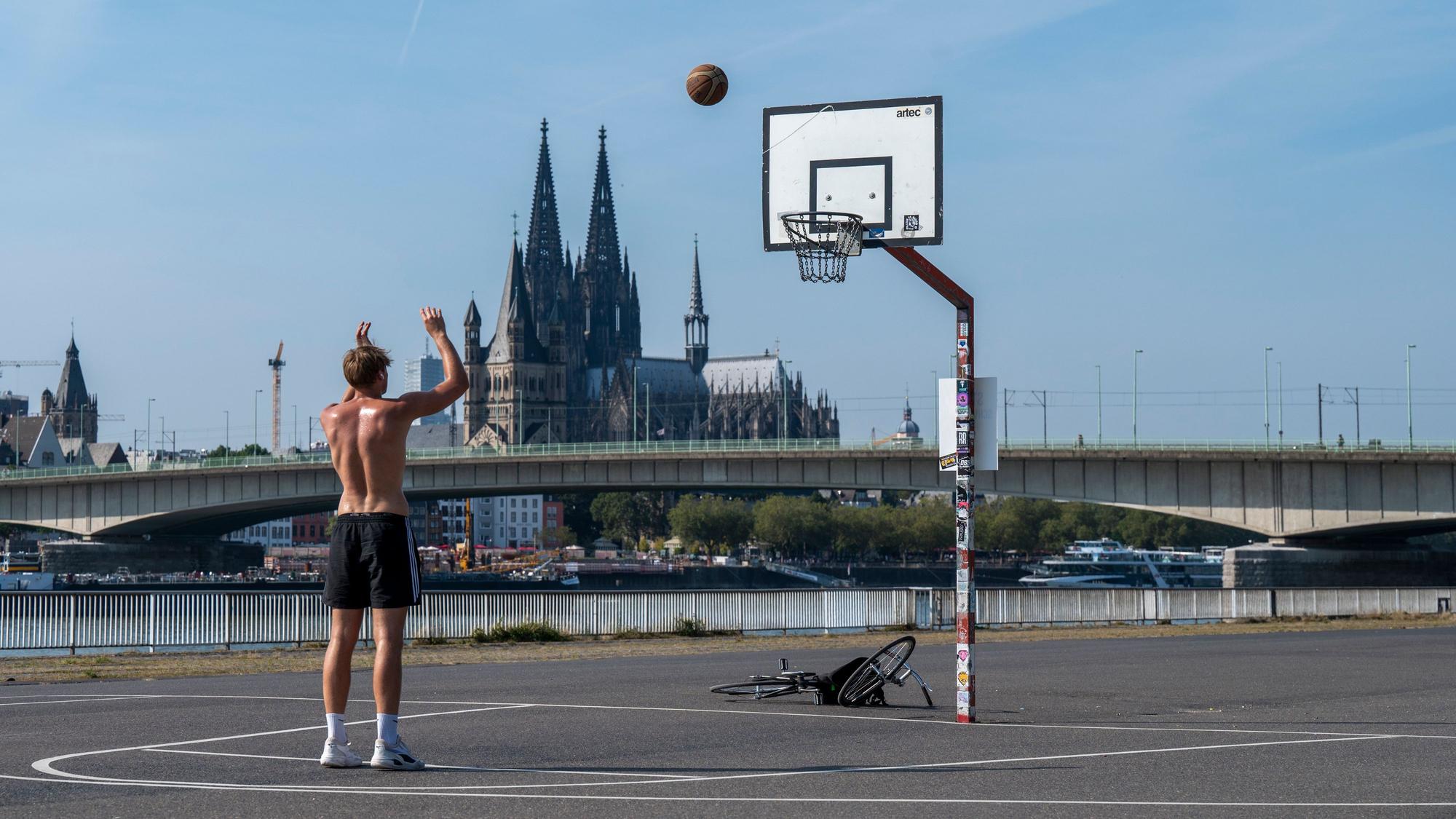 Junge zielt auf Basketballkorb, im Hintergrund der Kölner Dom.