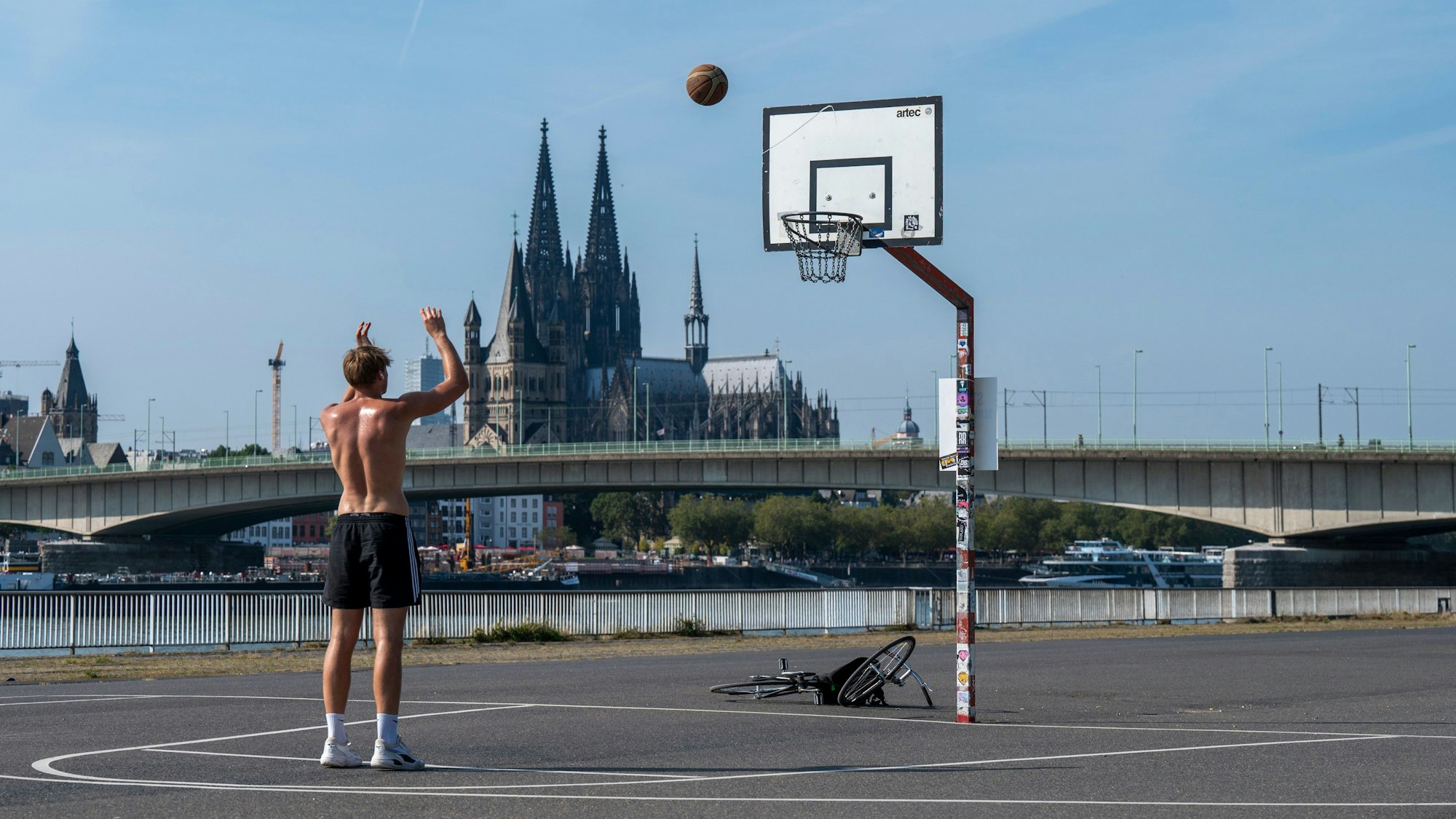 Junge zielt auf Basketballkorb, im Hintergrund der Kölner Dom.