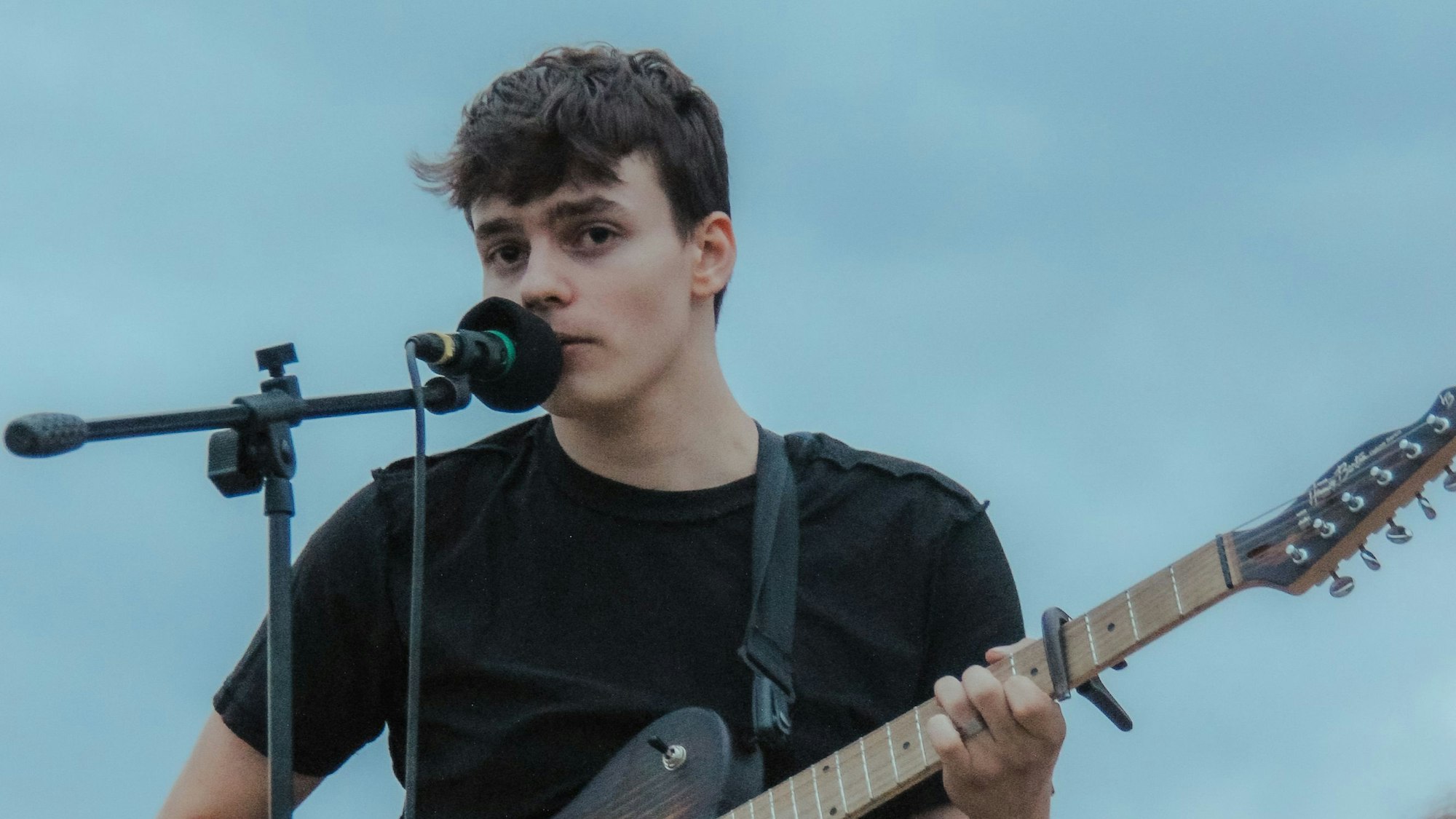 Ein junger Mann steht mit einer Gitarre an einem Mikrofon.