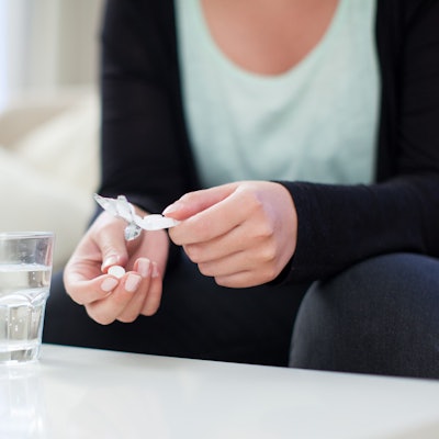 Eine Frau hält eine Tablette und eine Blisterpackung in der Hand. Vor ihr steht ein Glas Wasser.