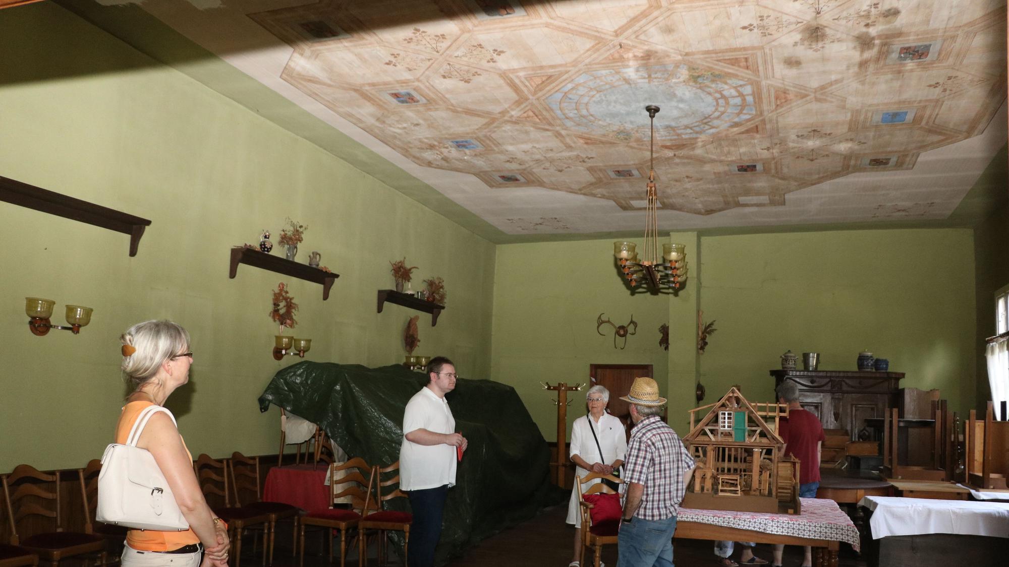 Ein Saal mit grünen Wänden und Deckenmalereien. Vier Leute besichtigen den Raum.