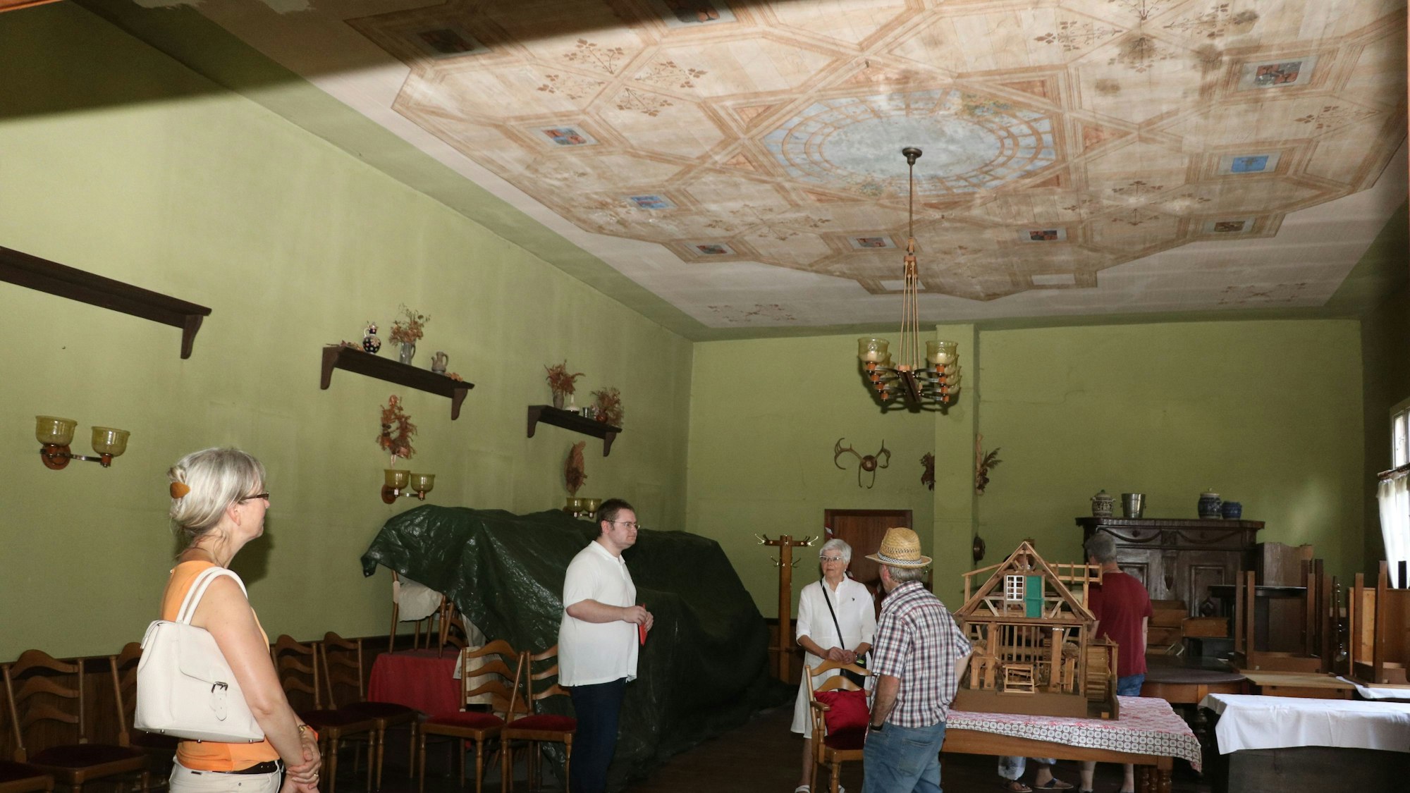 Ein Saal mit grünen Wänden und Deckenmalereien. Vier Leute besichtigen den Raum.