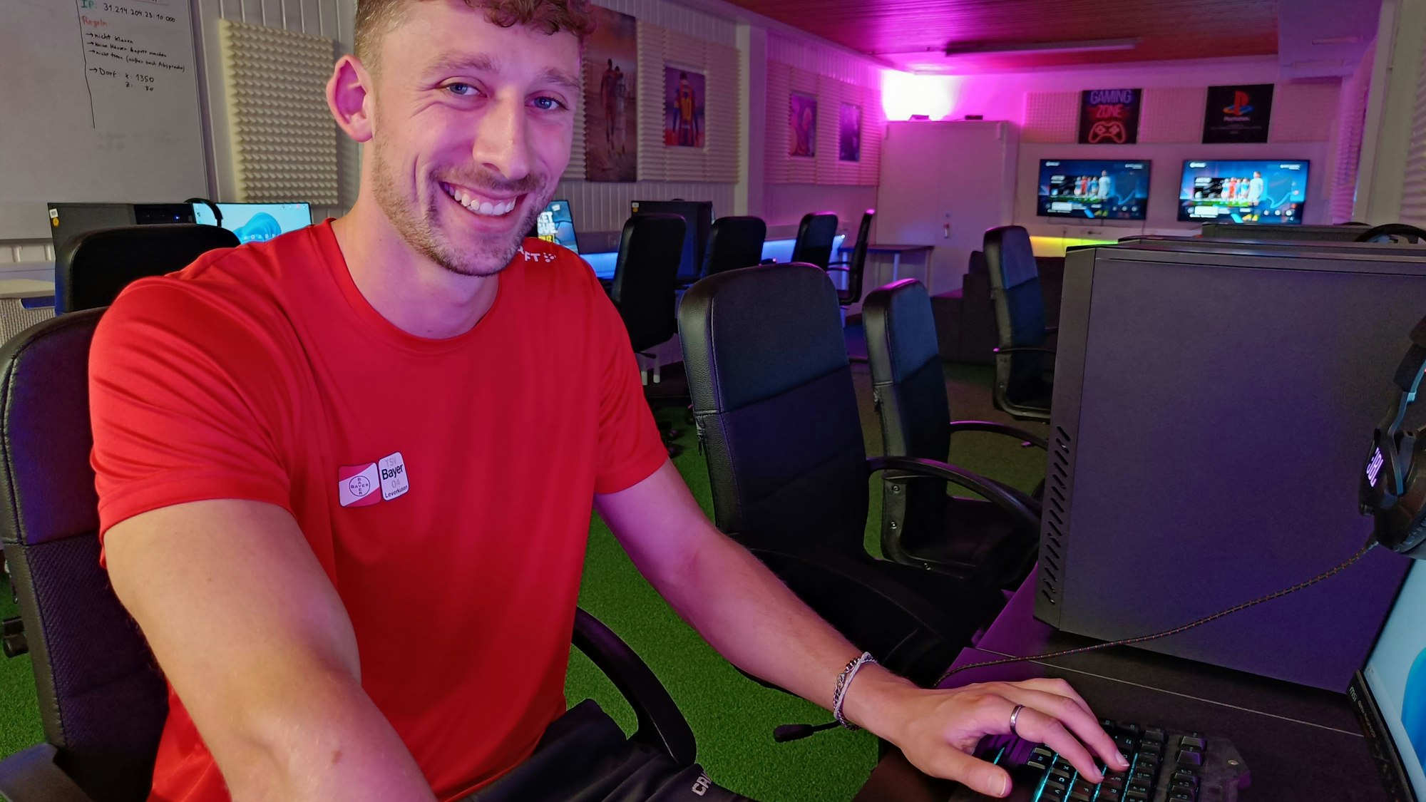 Ein junger Mann sitzt vor einem PC, die Hand an der Maus und Tastatur. Im Hintergrund sieht man LED-Lichter, die an der Wand befestigt sind und in verschiedenen Farben leuchten.