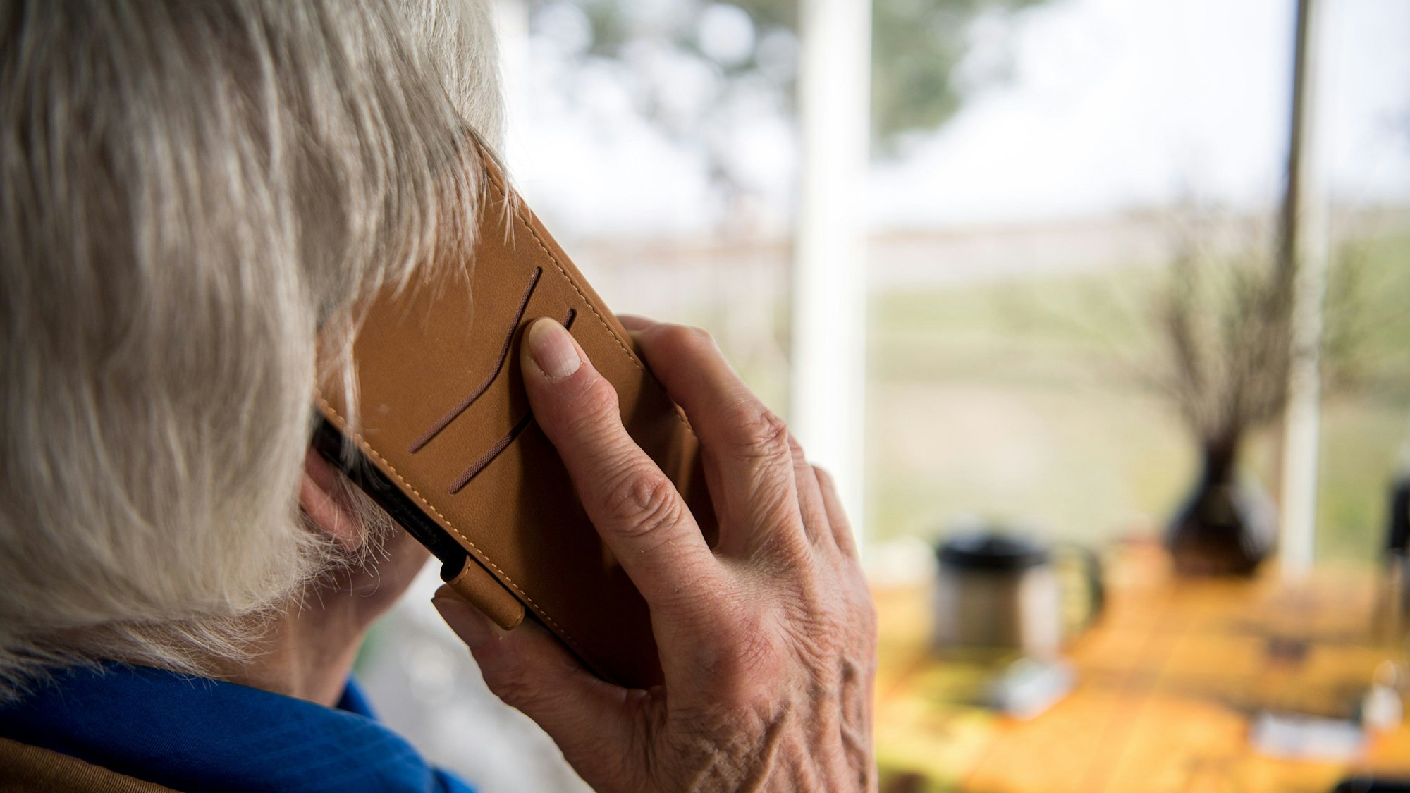 Eine Frau telefoniert mit einem Handy, das sich in einer Handyhülle befindet. Sie ist von hinten fotografiert worden.