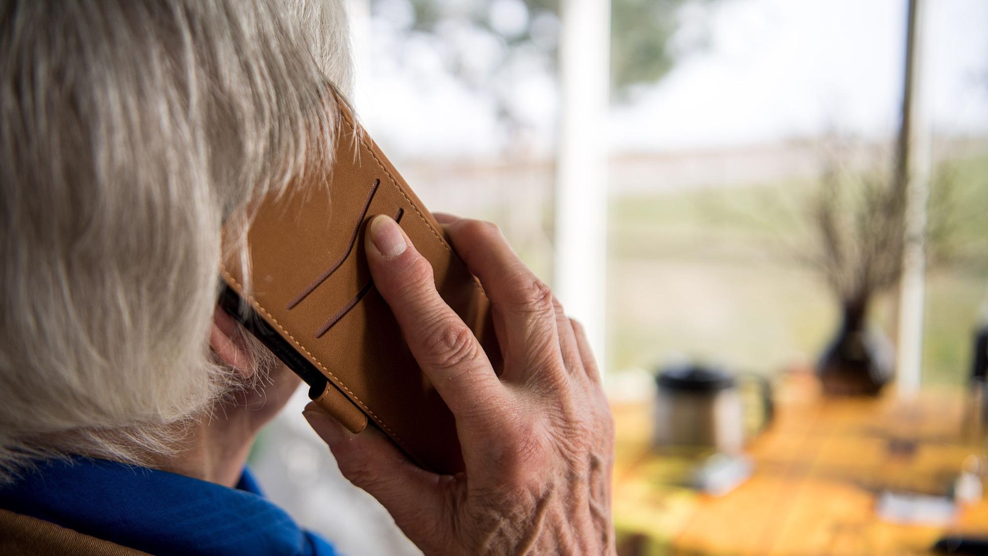 Ein Senior hält ein Telefon an sein Ohr. Man sieht den Mann nur von hinten.