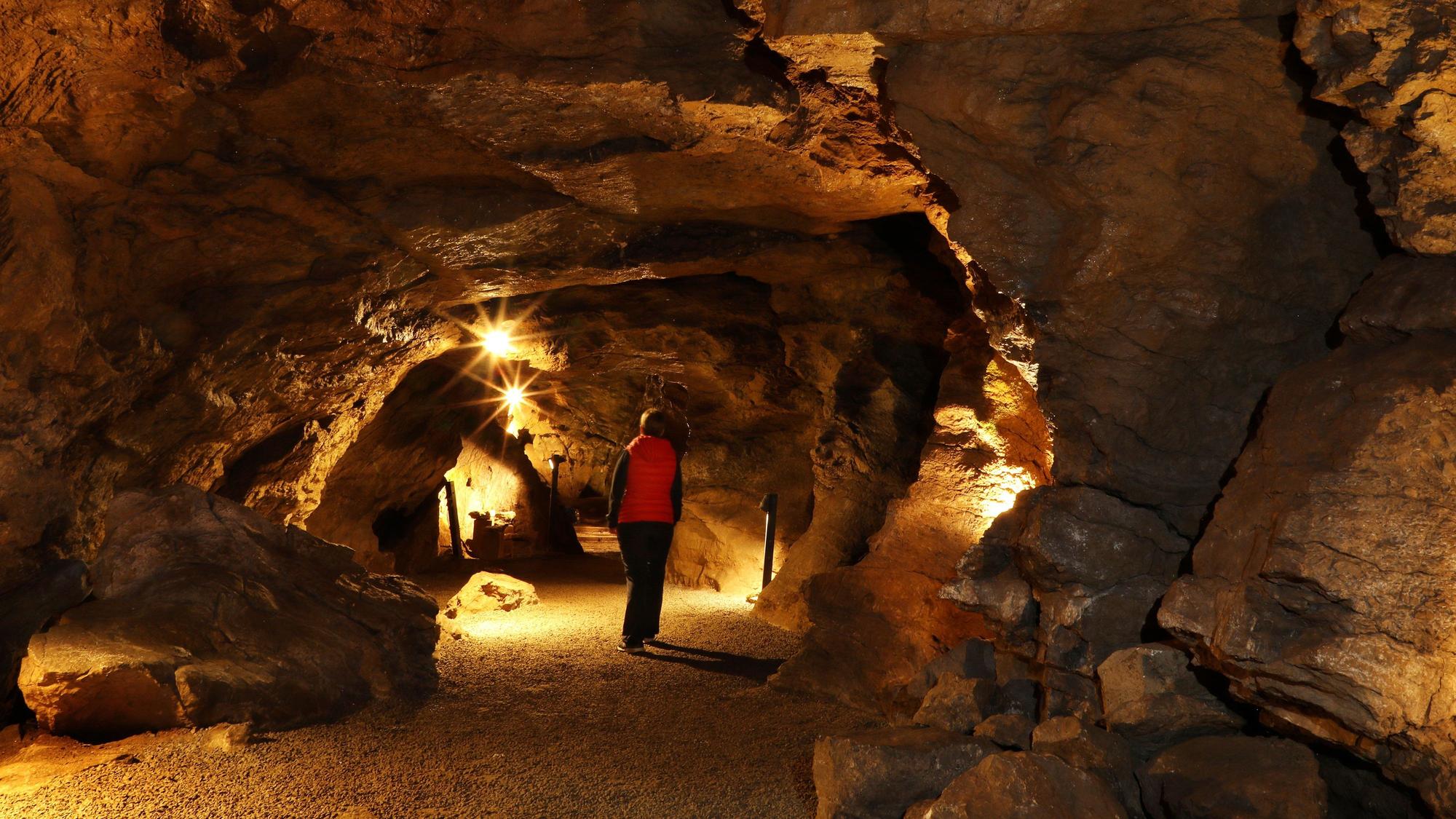 Eine Person in langer Hose und langem Pullover mit Weste in einer Höhle.