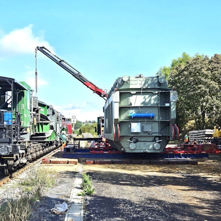 Ein Trafo (r.) für die Umspannanlage Dahlem ist am Bahnhof Kall angekommen und mit einem Kran vom Waggon abgeladen worden.