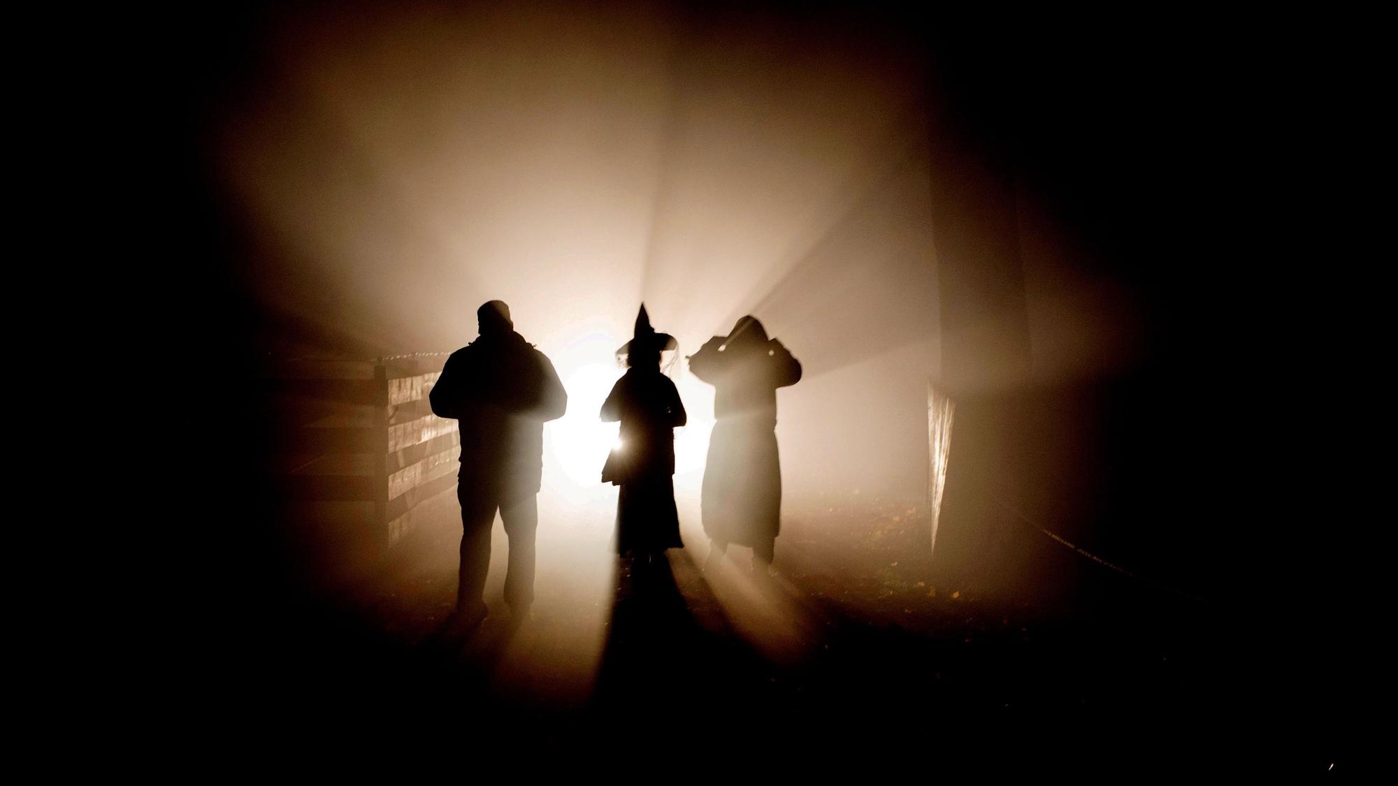 Im Gegenlicht treten gruselige Gestalten, eine mit Hexenhut, eine mit einer Kapuze der Kamera entgegen und sind nur als Silhouette zu sehen.