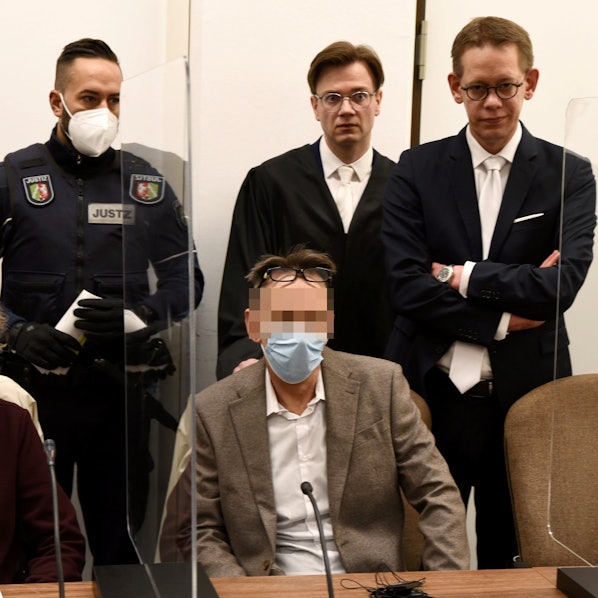 Der mutmaßliche Drach-Komplize Eugen W. sitzt im Gerichtssaal auf einem Stuhl. Hinter ihm stehen seine Verteidiger und ein Wachtmeister.