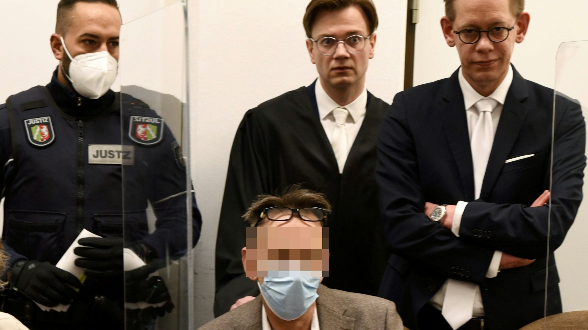 Der mutmaßliche Drach-Komplize Eugen W. sitzt im Gerichtssaal auf einem Stuhl. Hinter ihm stehen seine Verteidiger und ein Wachtmeister.