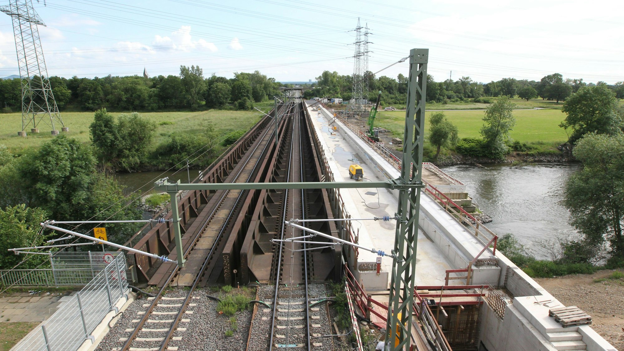 Eine Baustelle mit Bahngleisen für eine Brücke über einen Fluss.