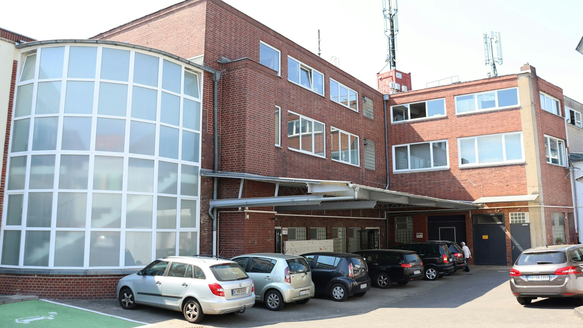 Vor einem Flach-Dach-Bau parken Autos.