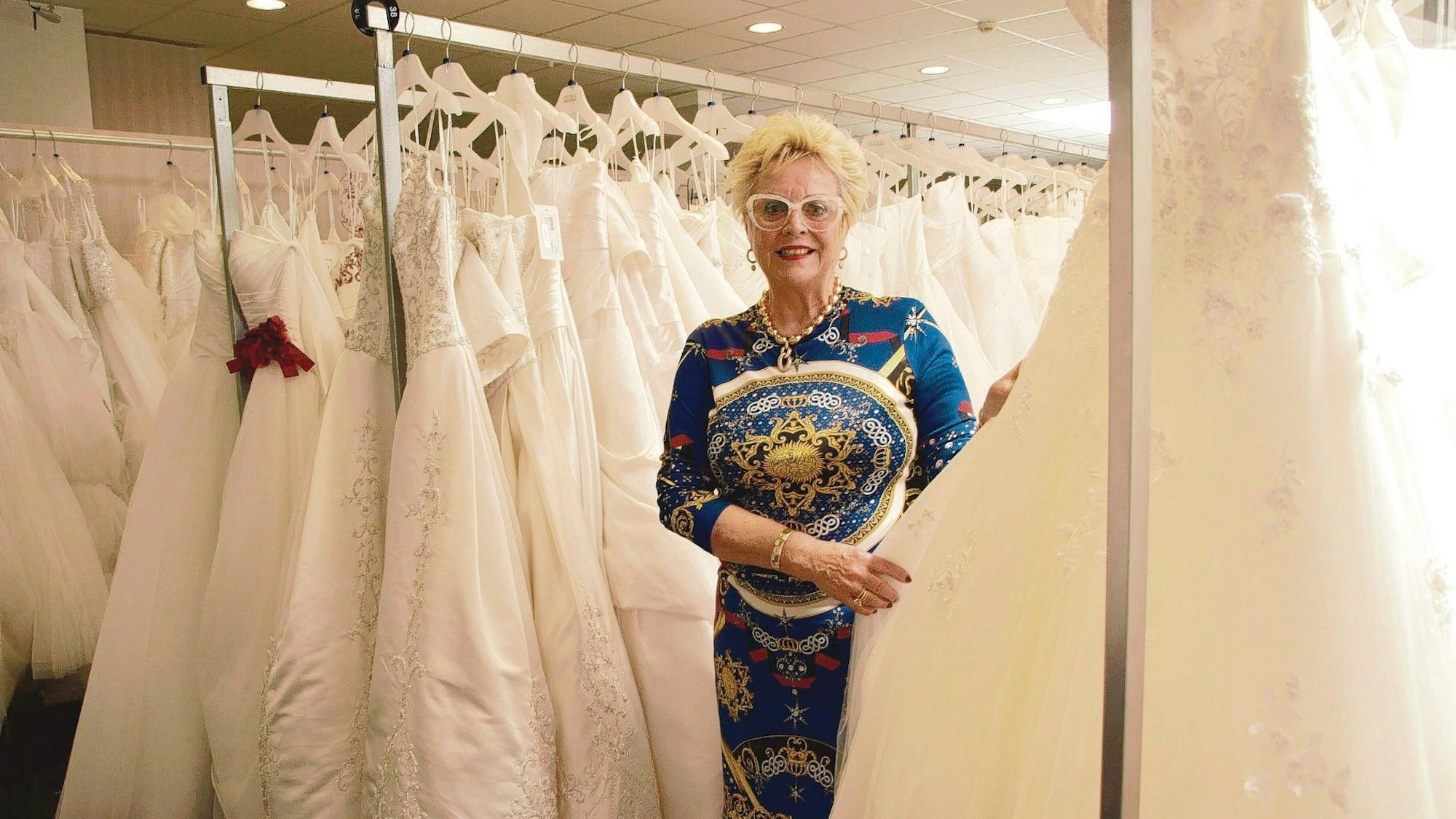 Maritta Emser mit Glitzerbrille in einem rosa Kleid. Hinter ihr eine schwarze Sponsorenwand.