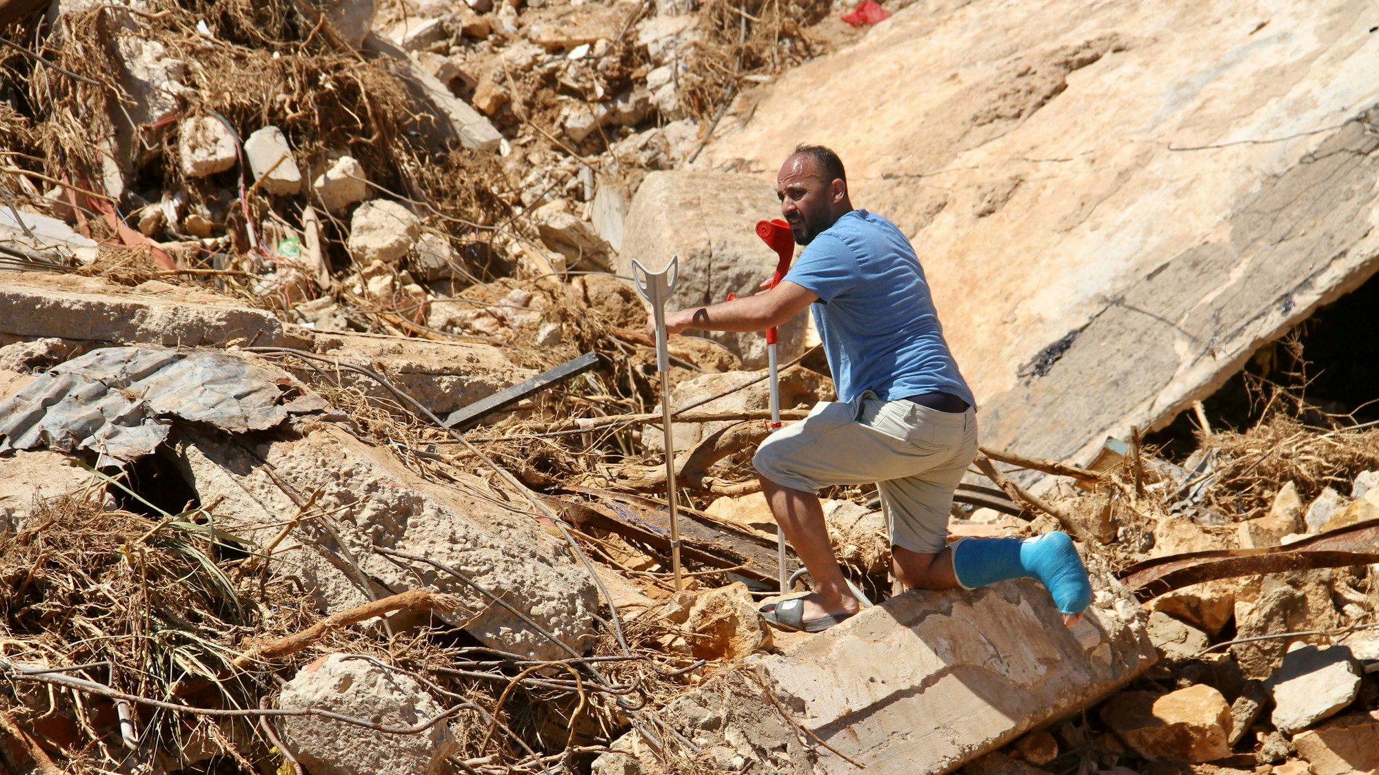 Ein Mann steigt an Krücken über Trümmer.