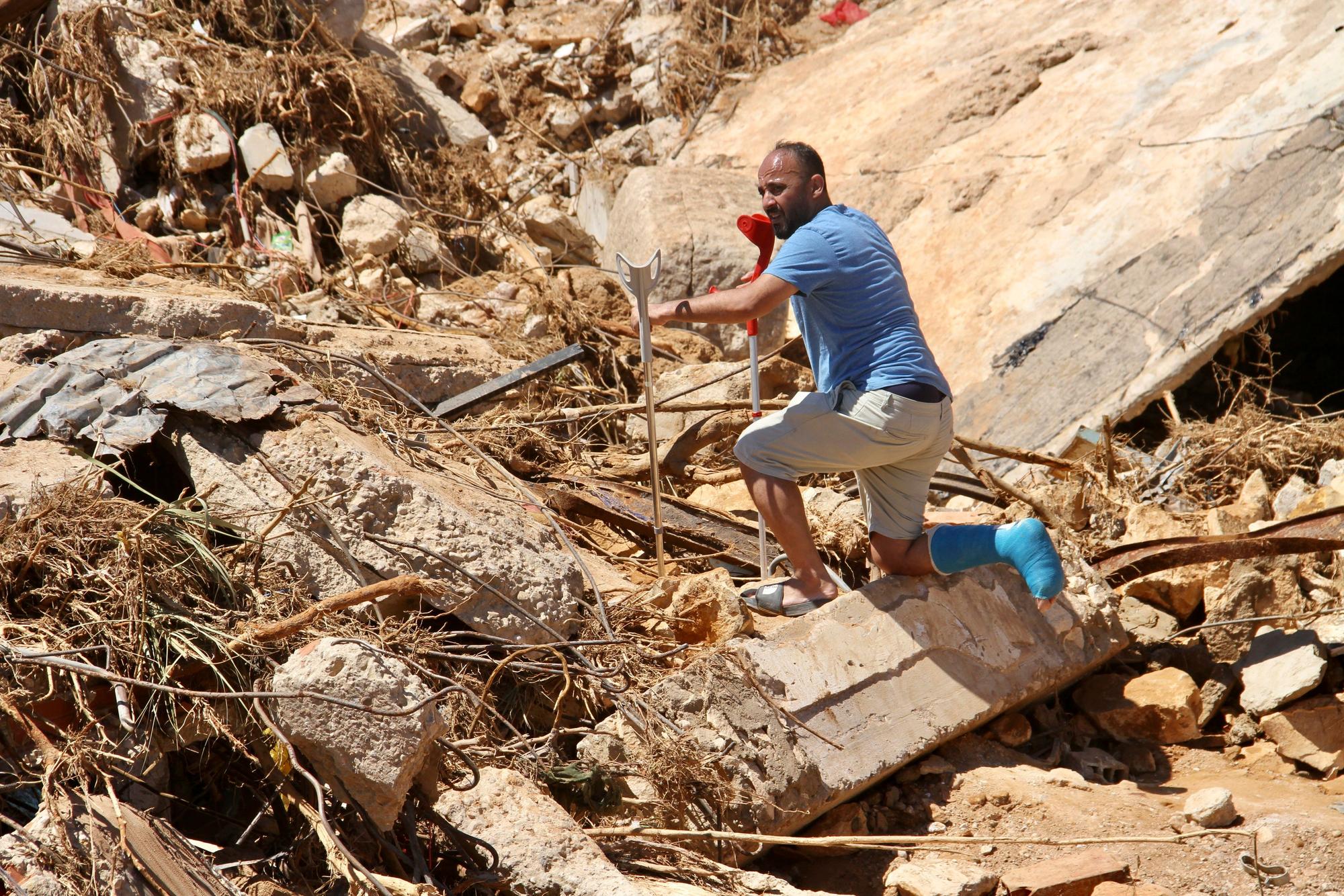13.09.2023, Libyen, Derna: Ein Mann steigt an Krücken über Trümmer. In Libyen herrscht nach den furchtbaren Überschwemmungen weiter der Ausnahmezustand. Allein in der schwer betroffenen Hafenstadt Darna werden Zehntausende von Toten befürchtet. Foto: Yousef Murad/AP/dpa +++ dpa-Bildfunk +++