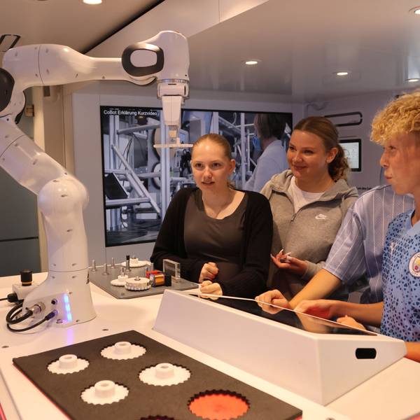 Drei Schüler bedienen über ein Eingabefeld den Arm eines Roboters.