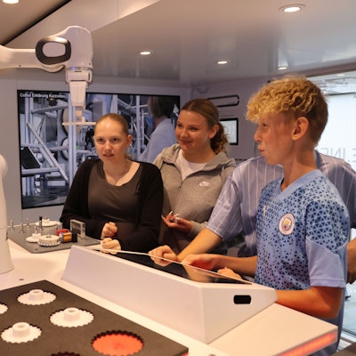 Drei Schüler bedienen über ein Eingabefeld den Arm eines Roboters.