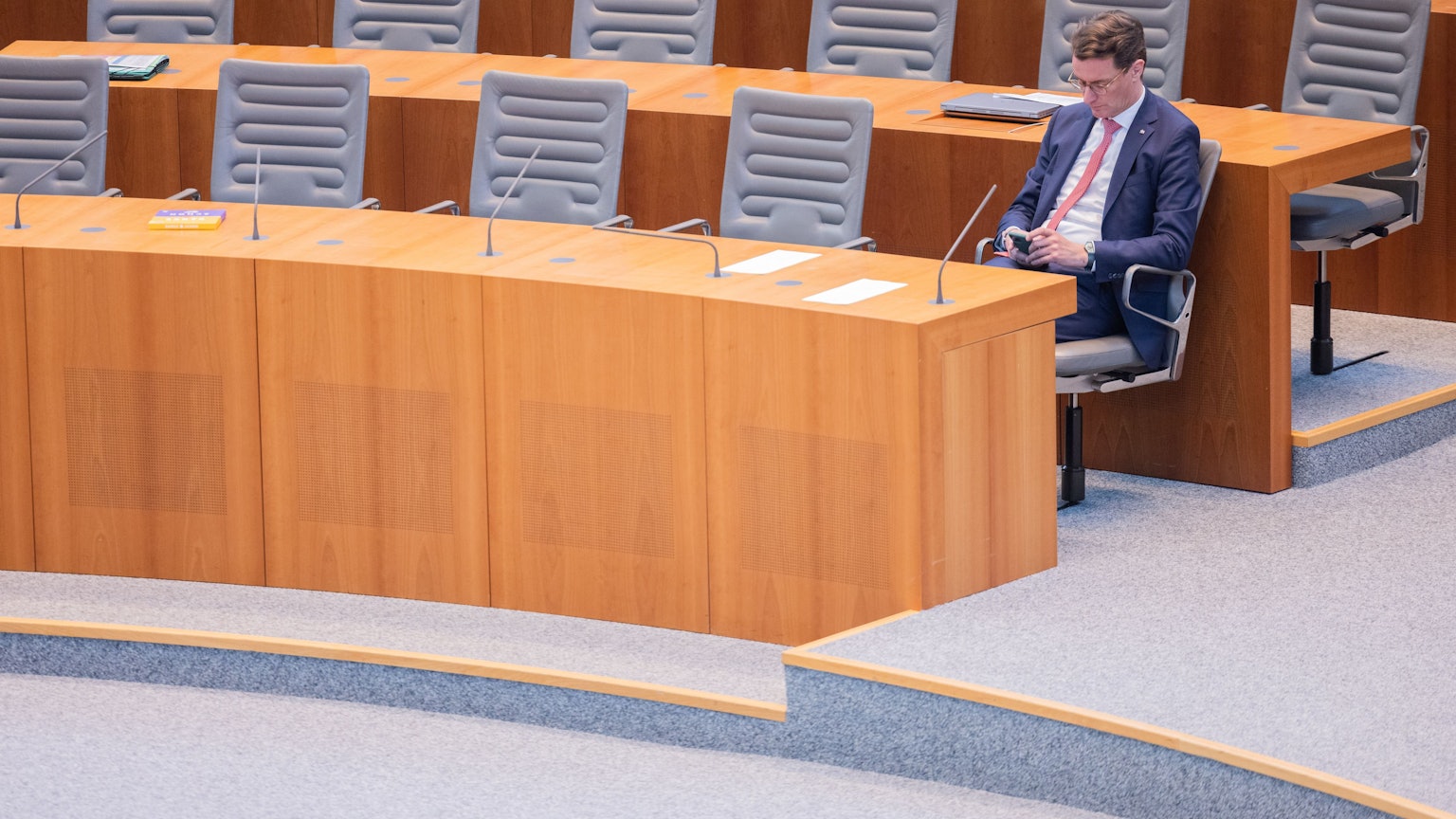 Hendrik Wüst (CDU), Ministerpräsident von Nordrhein-Westfalen, sitzt im Plenum des Landtags und schaut auf sein Handy.