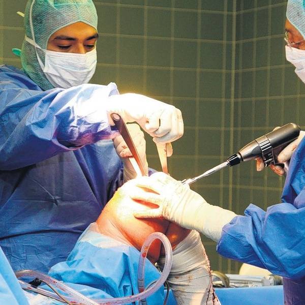Zwei Ärzte in OP-Kleidung, Masken und Hauben arbeiten an einem Knie.