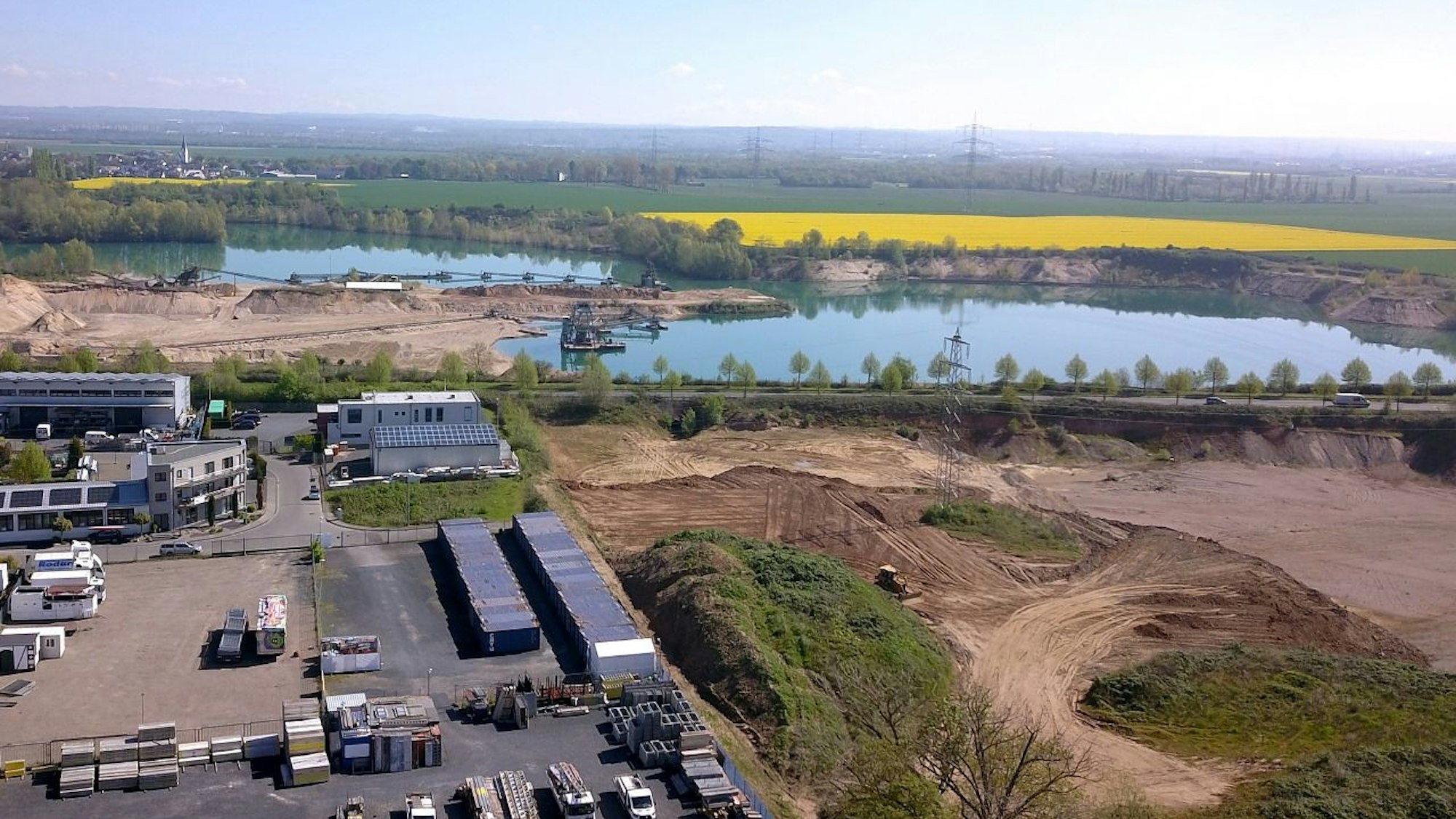 Die Luftaufnahme zeigt im Vordergrund das Niederkasseler Gewerbegebiet und im Hintergrund die mit Wasser gefüllten Kiesgruben.