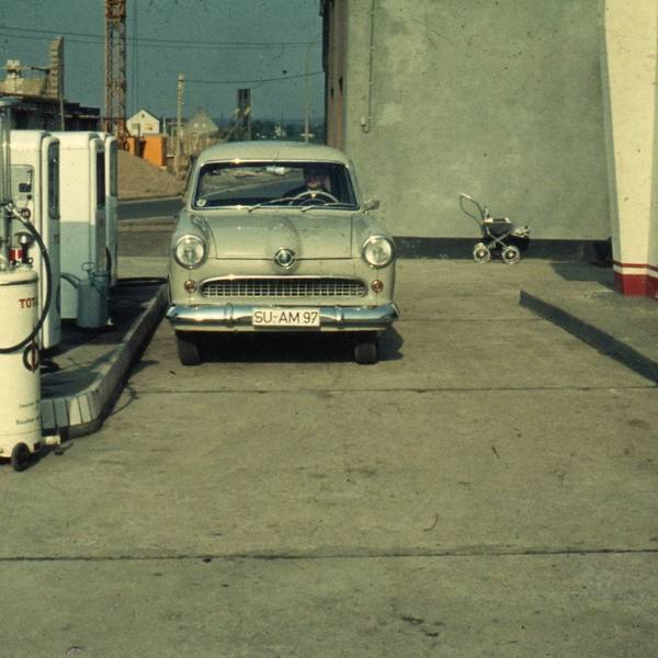 Anfang der 60er Jahre in Troisdorf. Ein Auto steht an einer Tankstelle ohne Überdachung, im Hintergrund sieht man eine Baustelle.