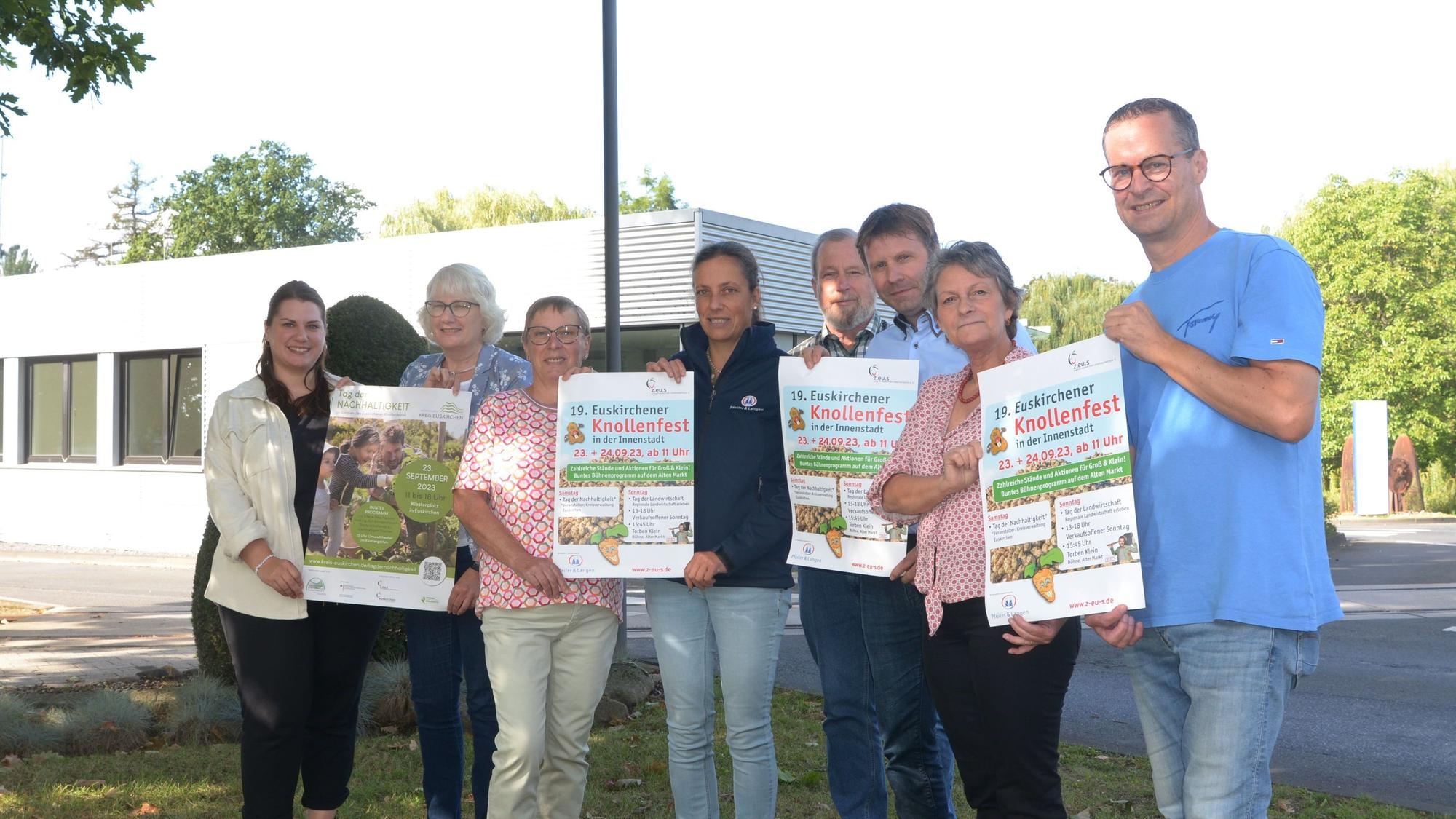 Acht Frauen und Männer, die das Euskirchener Knollenfest vorbereiten, stehen in einer Reihe. Sie zeigen Werbeplakate für die Großveranstaltung.