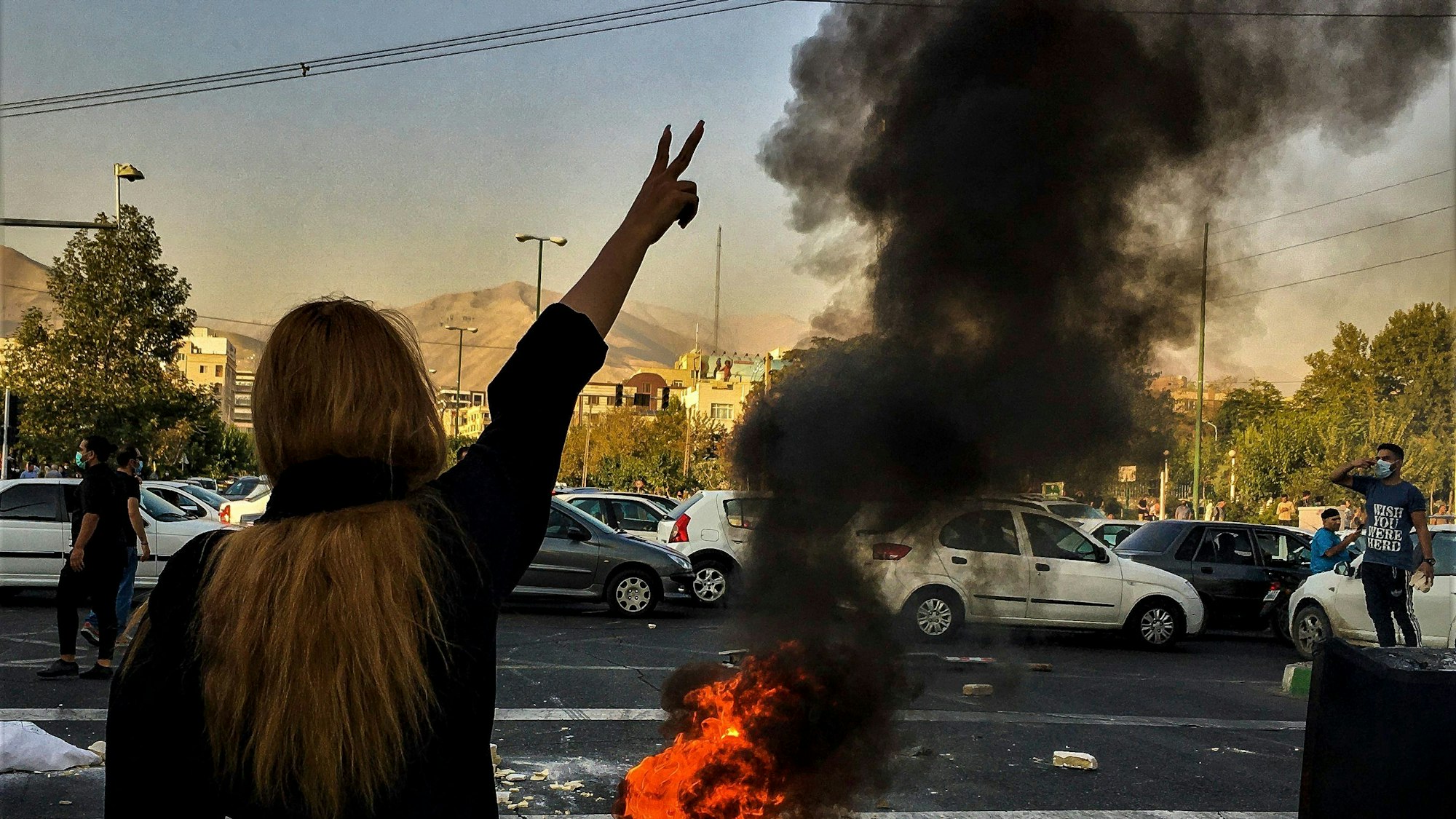 Eine Frau steht während einer Demonstration im Iran nach dem Tod der 22-jährigen Mahsa Amini vor einem brennenden Autoreifen und zeigt das Victory-Zeichen.