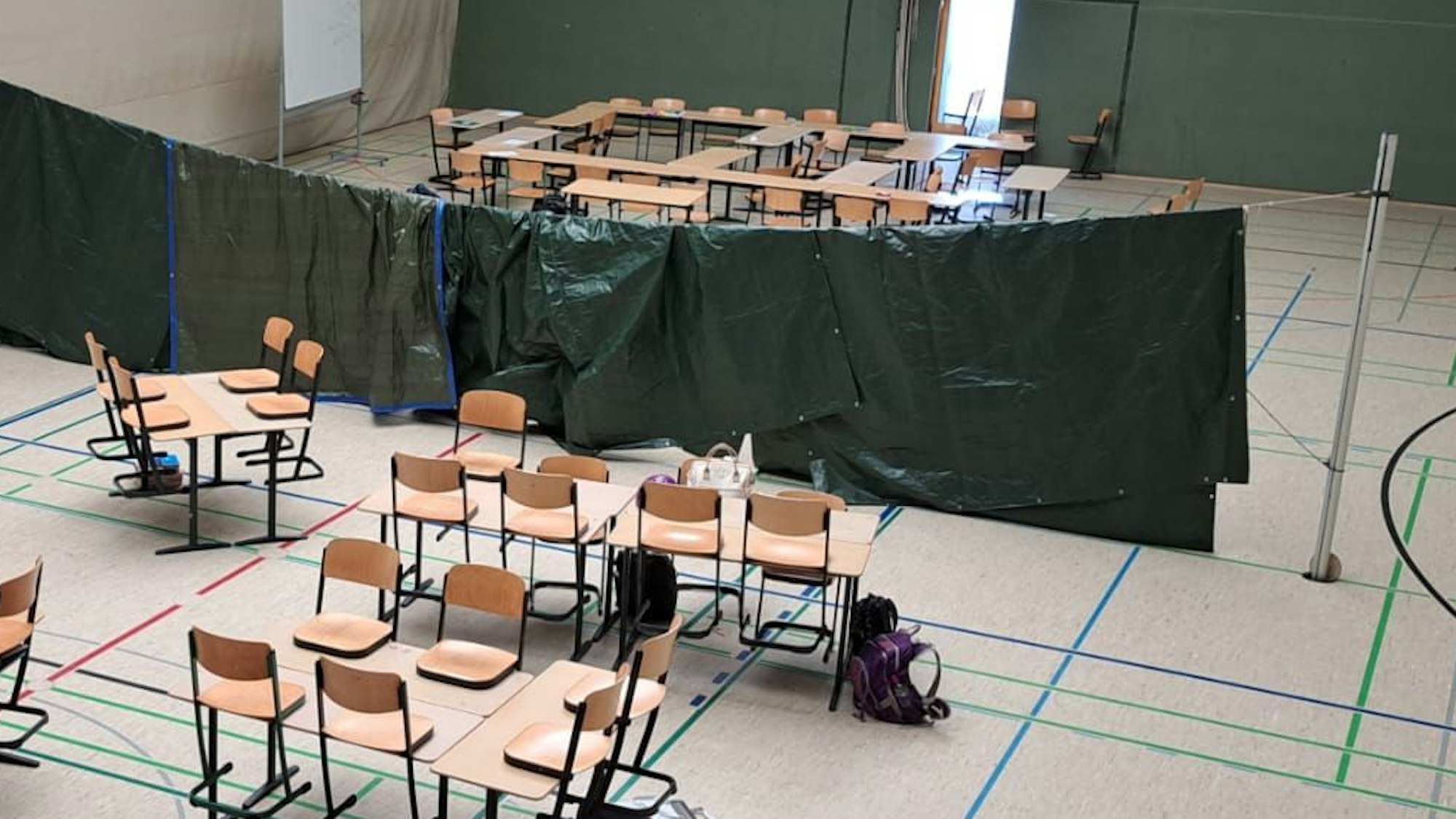 Das Bild zeigt die Turnhalle der Gesamtschule. In der Halle stehen Tische und Stühle. Die einzelnen Klassen sind mit schwarzen Tüchern abgetrennt, die auf Volleyballnetzen aufgehängt wurden.