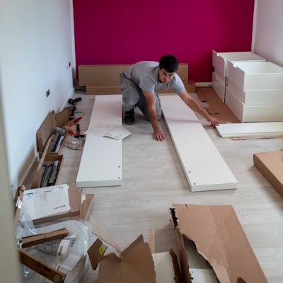 Das Bild zeigt einen Handwerker, wie er einen Schrank zusammenbaut.