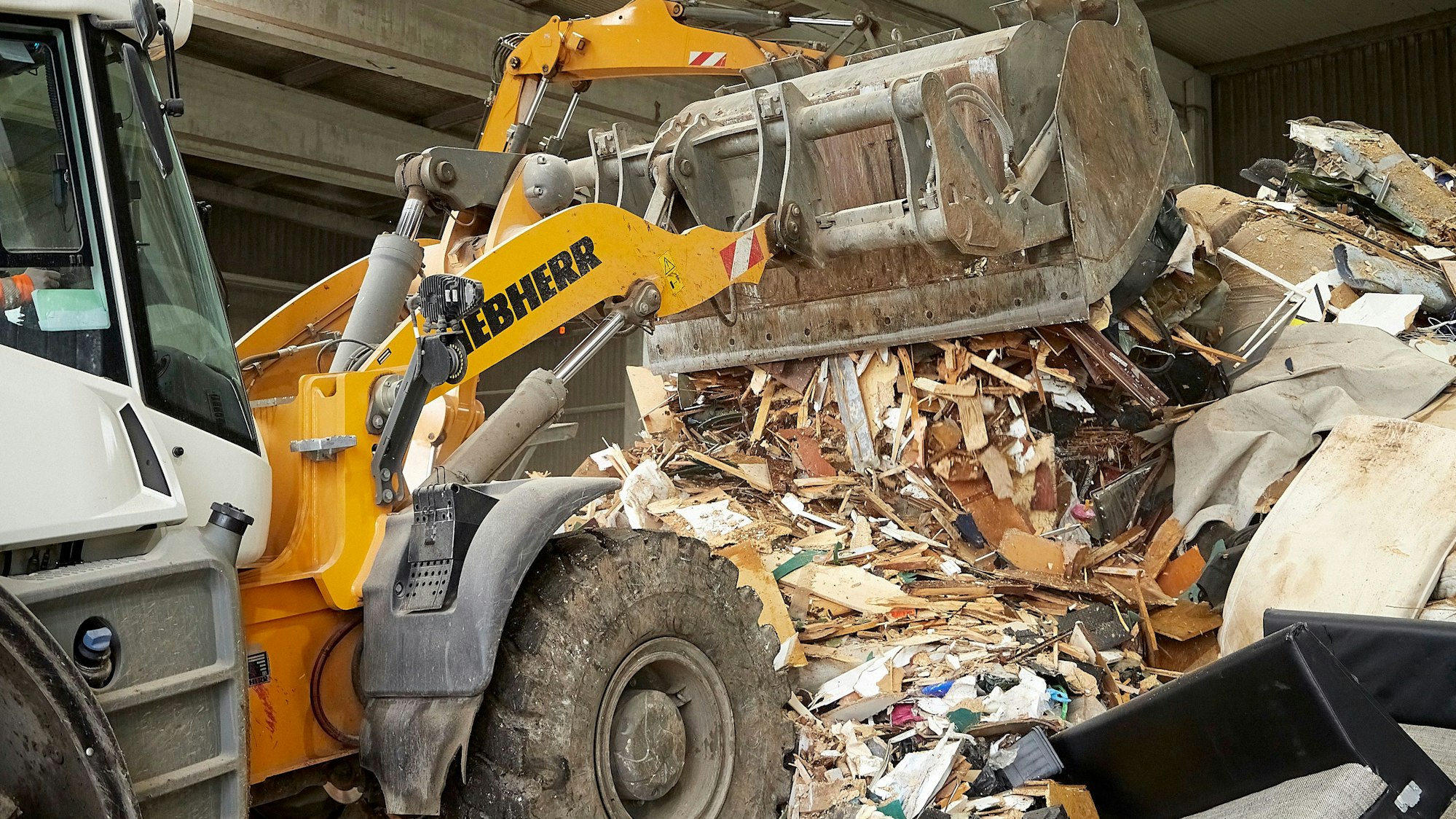 Das Bild zeigt einen Bagger, der mithilfe seiner Schaufel den Berg an Hausmüll aufschüttet.