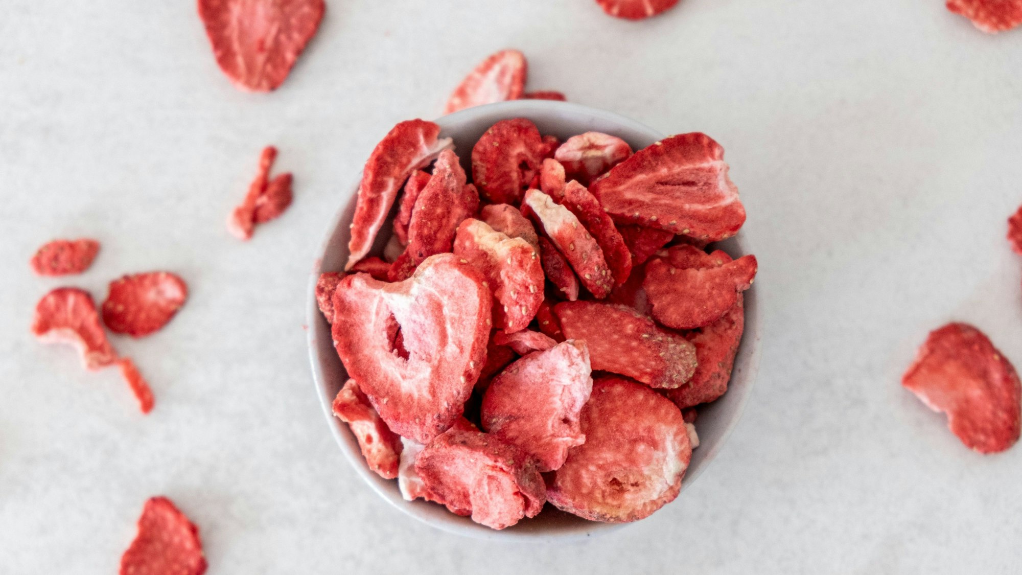 Gefriergetrocknete Erdbeeren in einer Schüssel und verstreut darum herum auf dem Tisch
