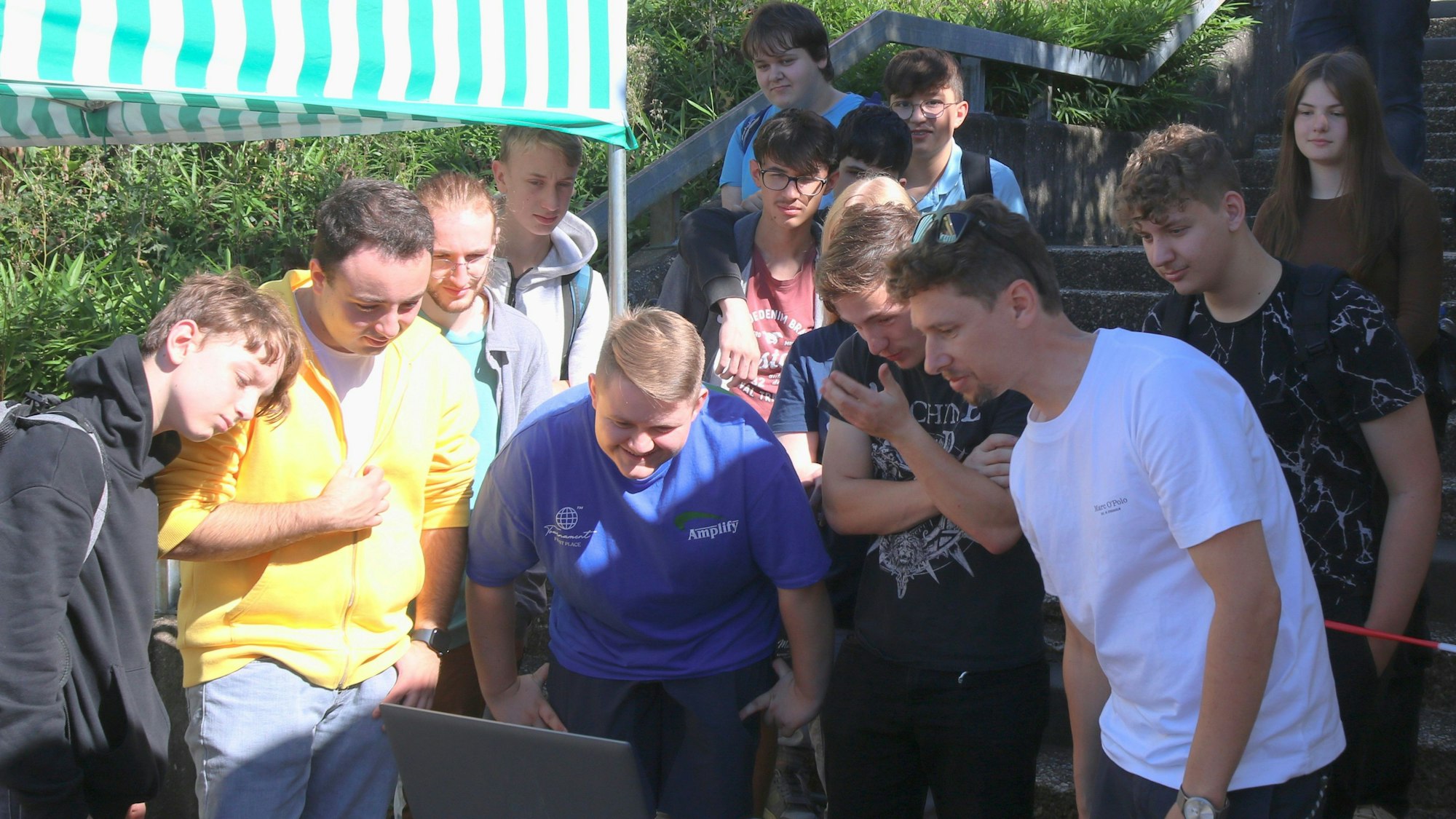 Die Jugendlichen der städtischen Gesamtschule stehen zusammen und schauen alle auf den Bildschirm eines Laptops.