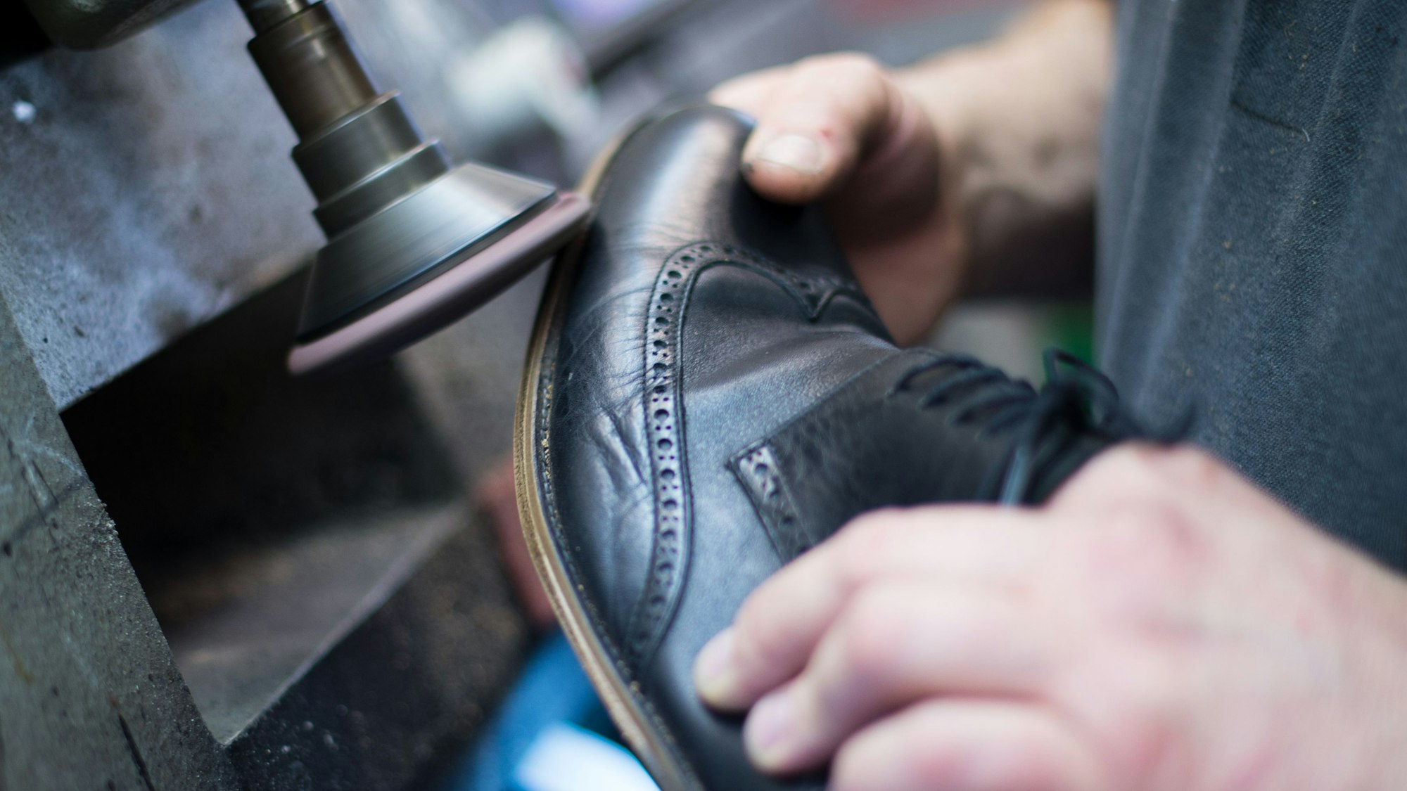 Die Schuhsohle eines schwarzen Lederschuhs wird an einer Maschine abgeschliffen.