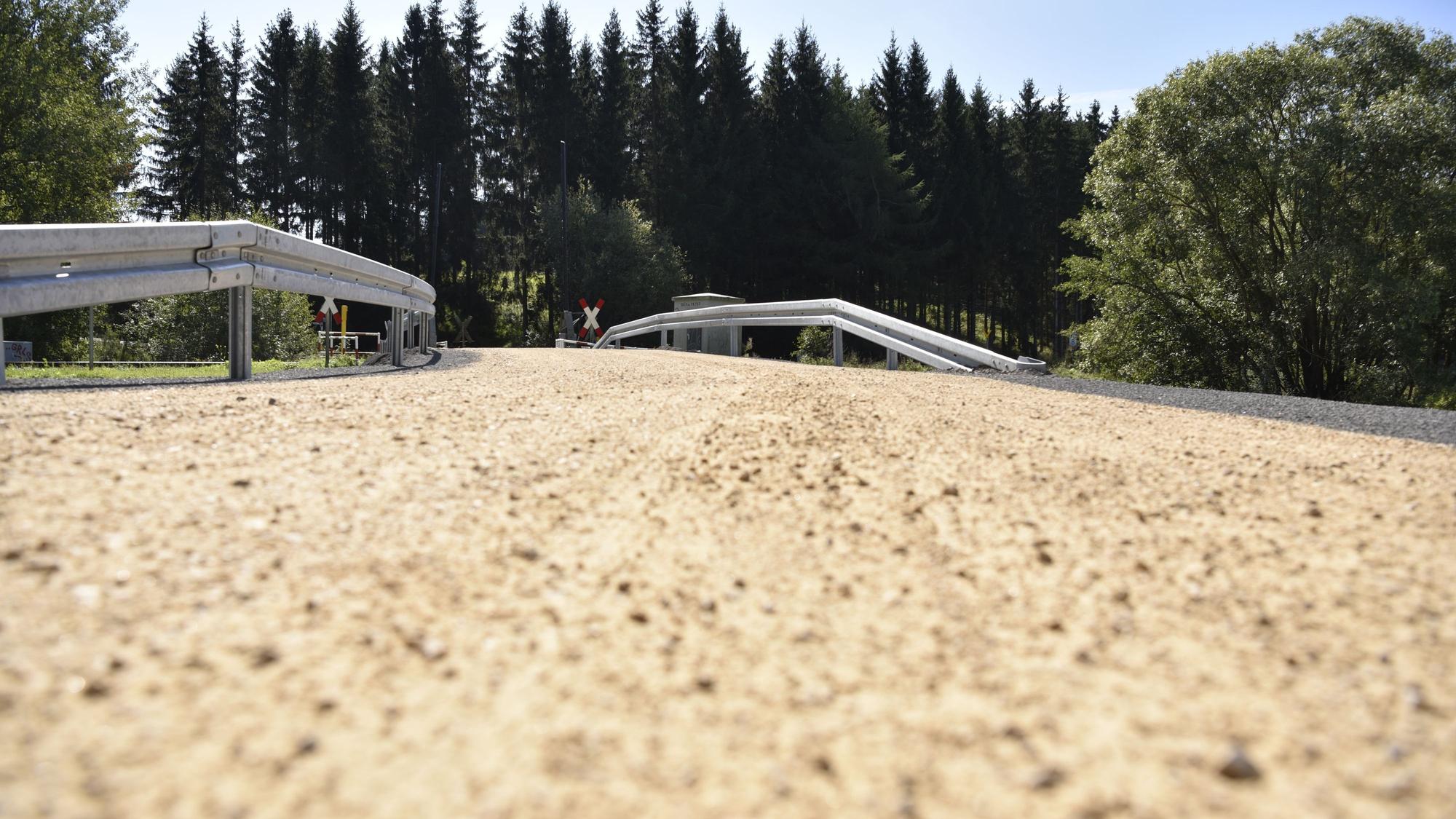 Der Weg führt über eine Brücke in Richtung Wald.
