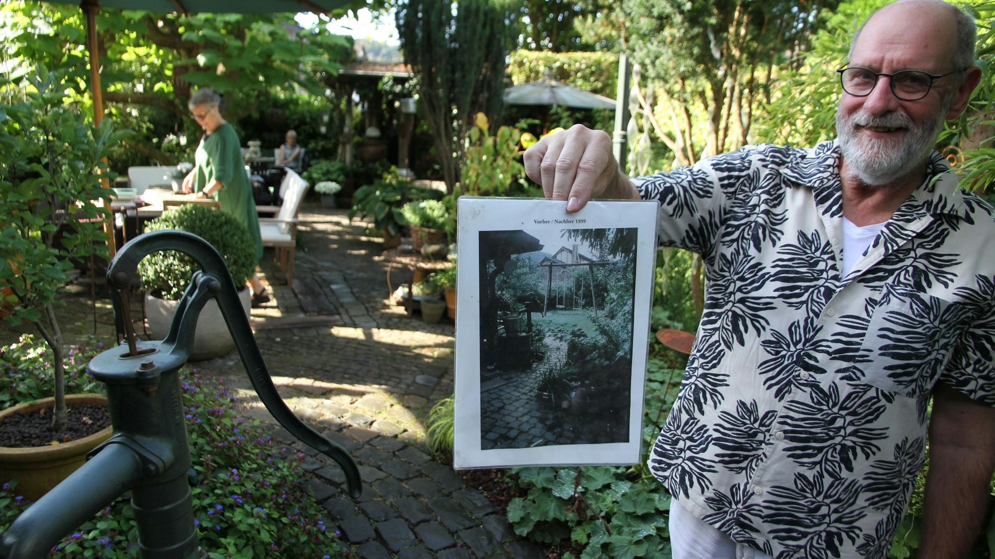 Bergische Gartentour 2023, offene Gärten, Michael Panthen in Lohmar-Neuhonrath hält ein Foto von seinem Garten vor der Umgestaltung in die Kamera