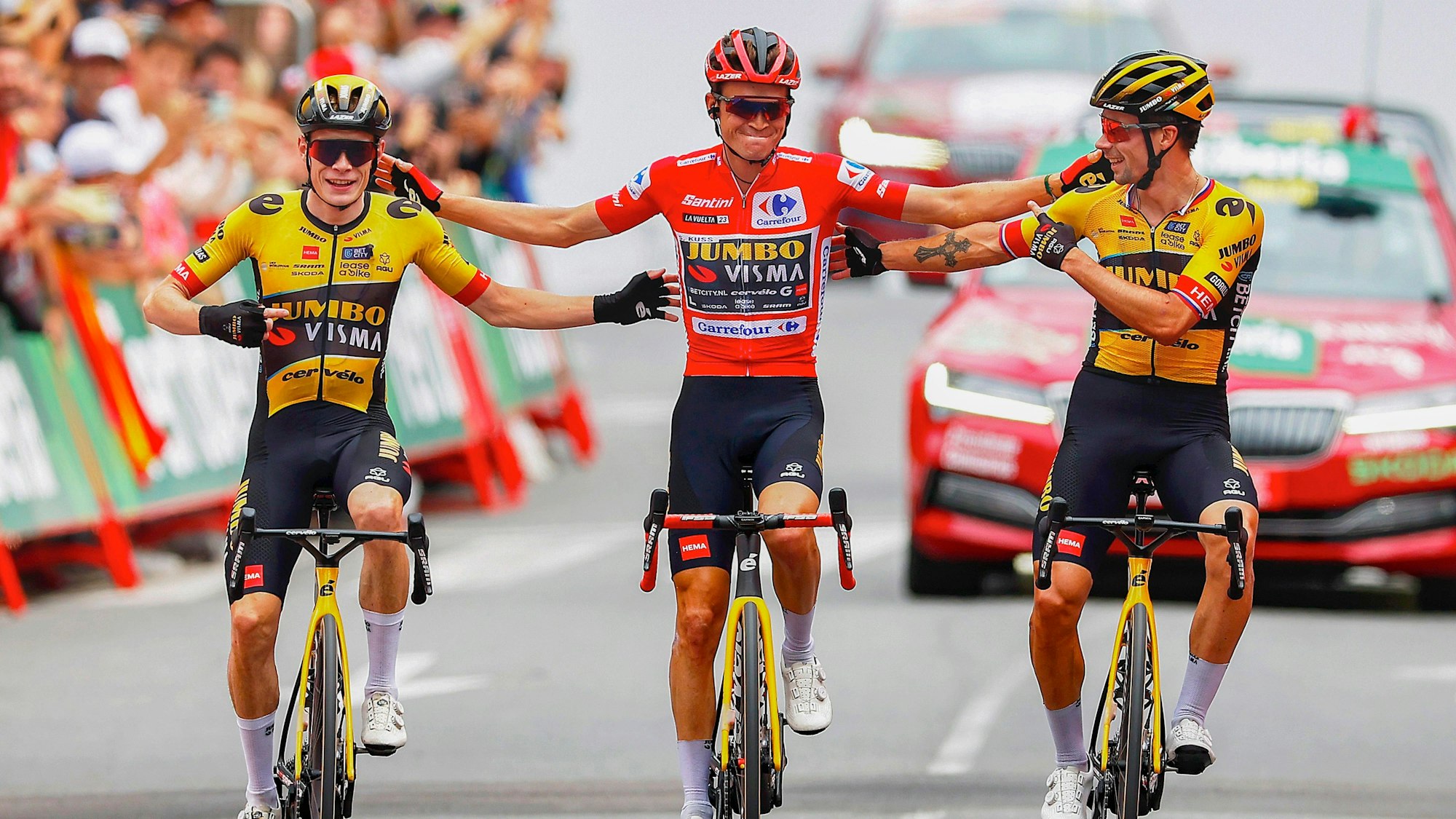 Jonas Vingegaard (links) und Primoz Roglic (rechts) nehmen den Vuelta-Sieger Sepp Kuss in ihre Mitte. Alle drei Profis fahren für Jumbo-Visma.