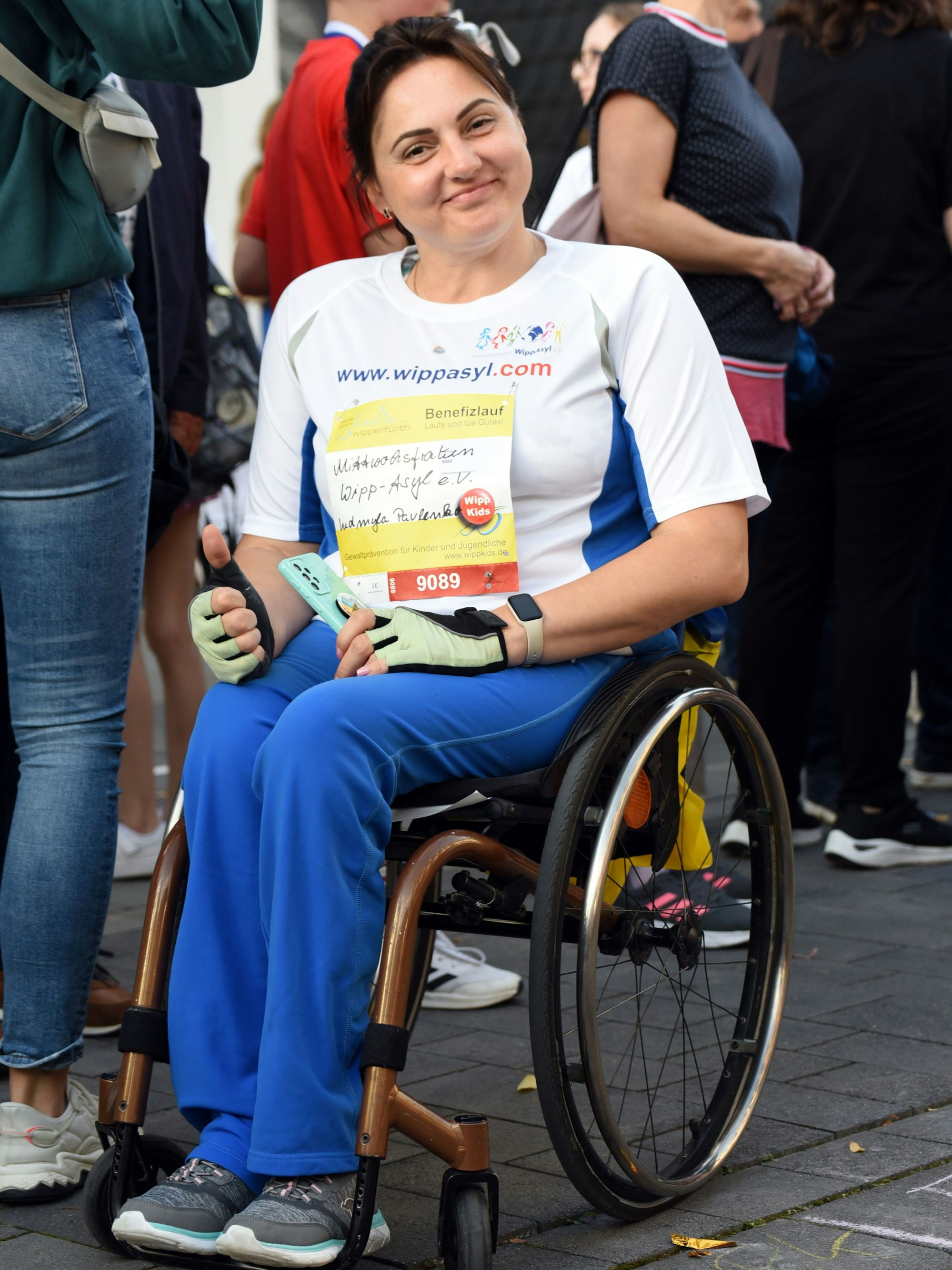 Eine Frau in Sportbekleidung sitzt in einem Rollstuhl und hält eine Urkunde in den Händen.